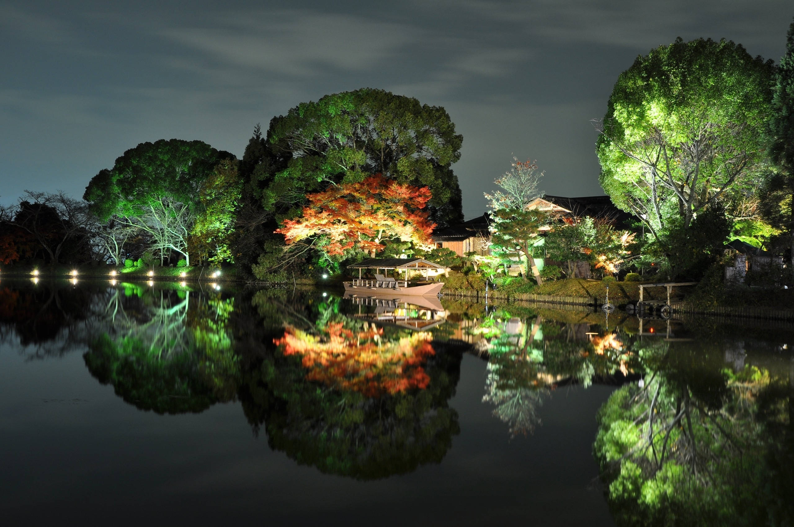 日本 桌布 壁紙 — 日本花園的寧靜夜景，燈光照亮的樹木倒映在平靜的水面上。