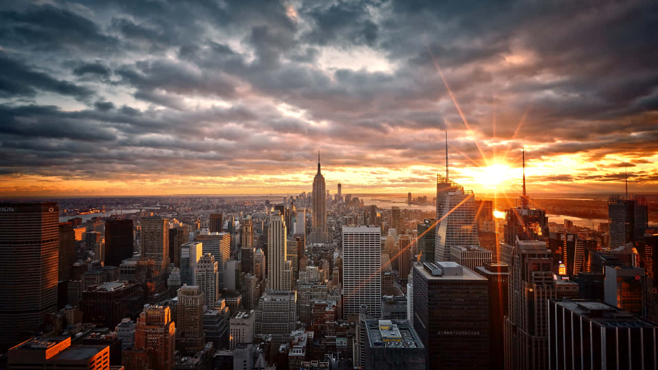 720p Empire State Building 桌布 壁紙 — 日落將紐約市的天際線沐浴在金黃色的光芒中，雲彩劃過戲劇性的天空。