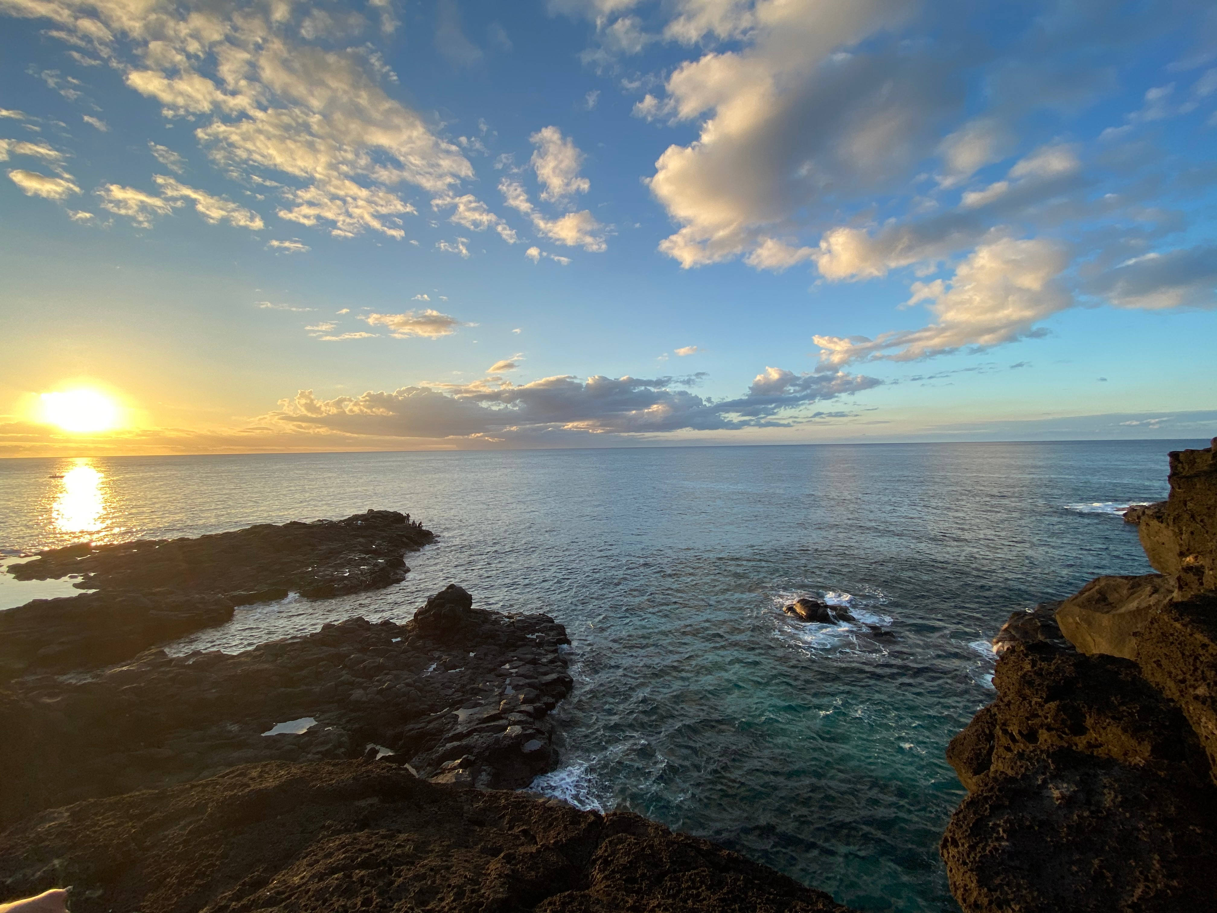Mauritius 桌布 壁紙 — 日落於岩石海岸線，金色光芒映照在碧綠海水和散落的雲朵上。