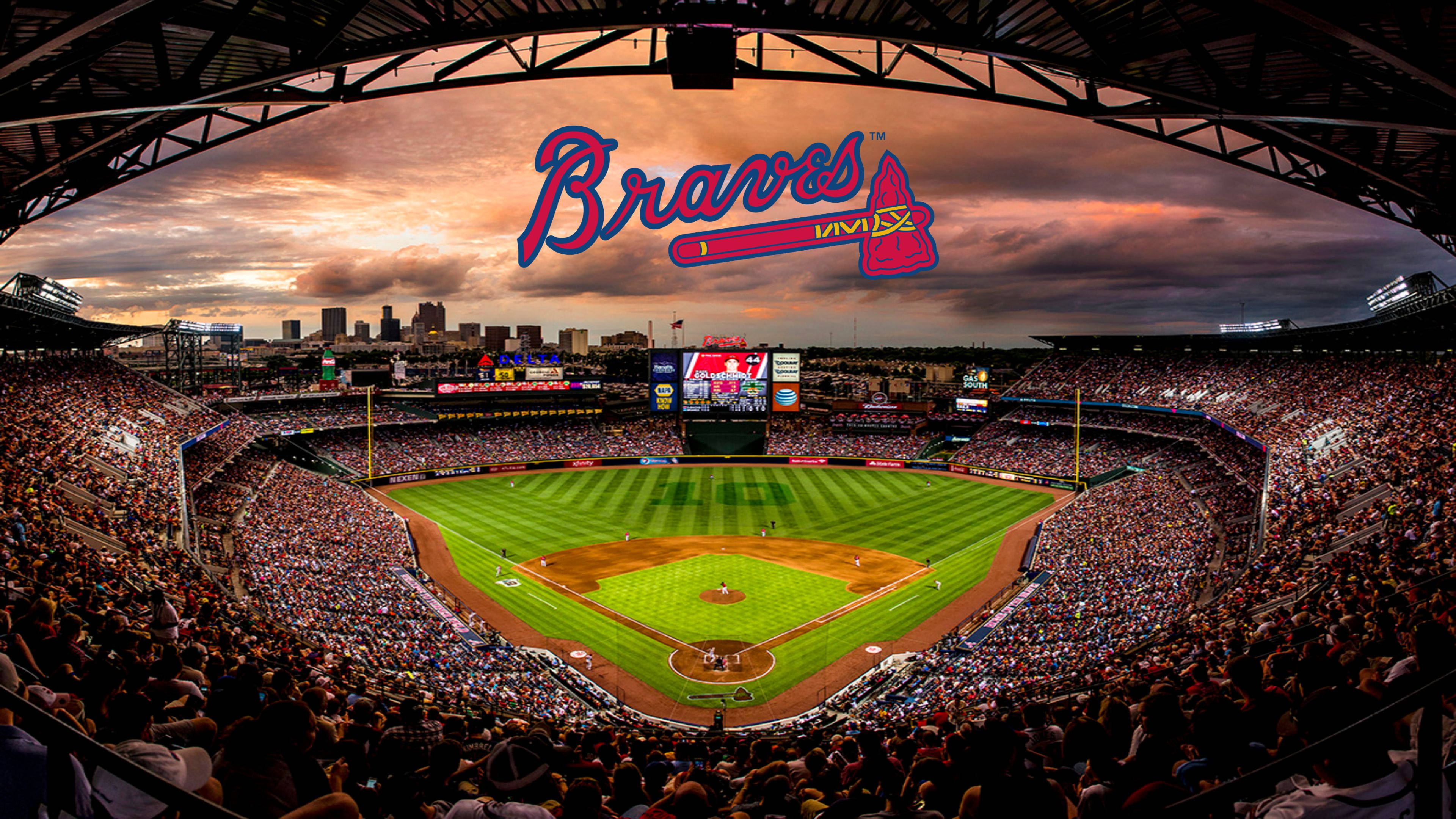 Braves 桌布 壁紙 — 日落時分，一個擠滿觀眾的棒球場全景，勇士隊標誌在球場上方發光。