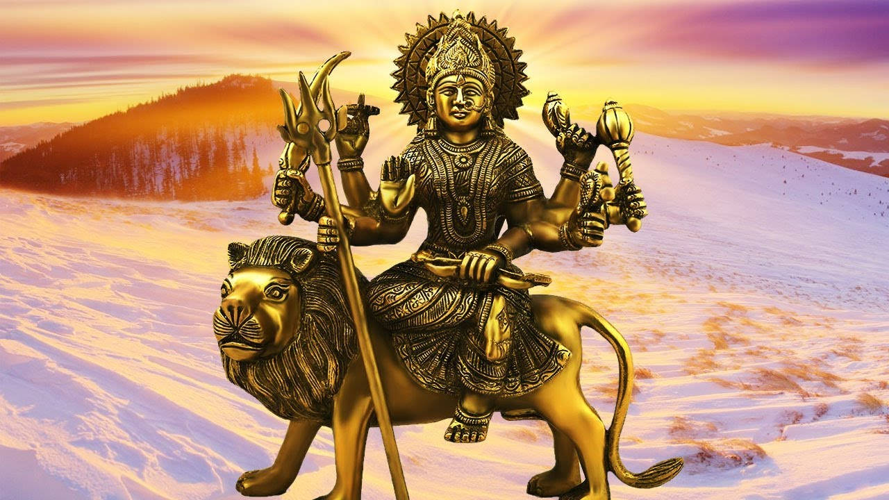 Vaishno Devi 桌布 壁紙 — 日落時分，一尊多臂神祇騎著獅子穿越雪山山脈的金色雕像。
