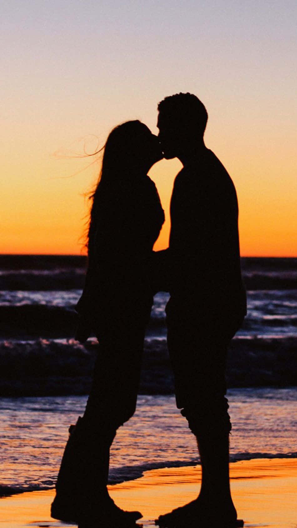 couples kissing 桌布 壁紙 — 日落時分，一對情侶在沙灘上接吻的剪影，伴隨橙色的天空和溫柔的海浪。