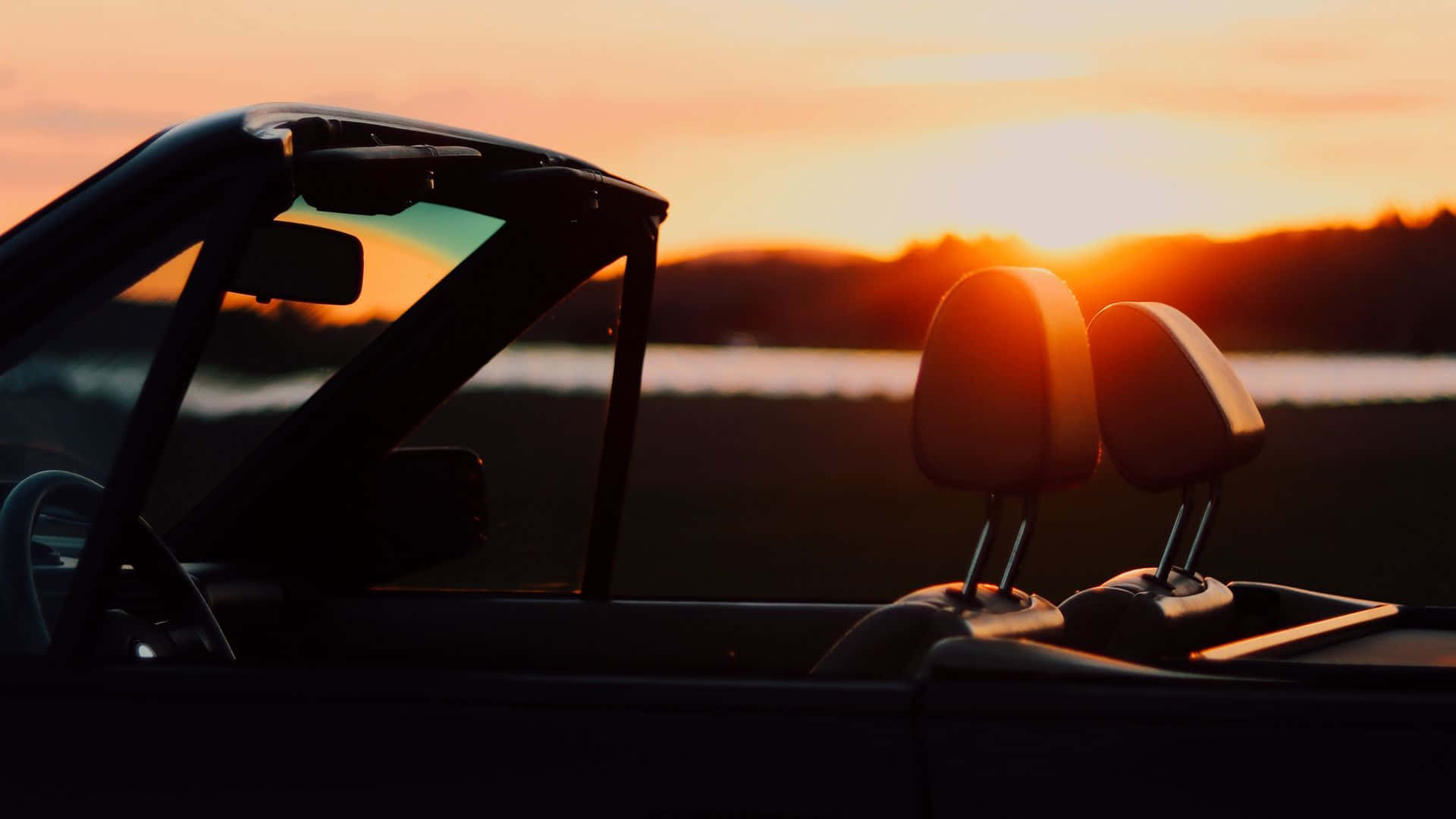 Sunset Drive 桌布 壁紙 — 日落時分，一輛敞篷車的剪影，伴隨發光的橙色天空和遠處的水面。
