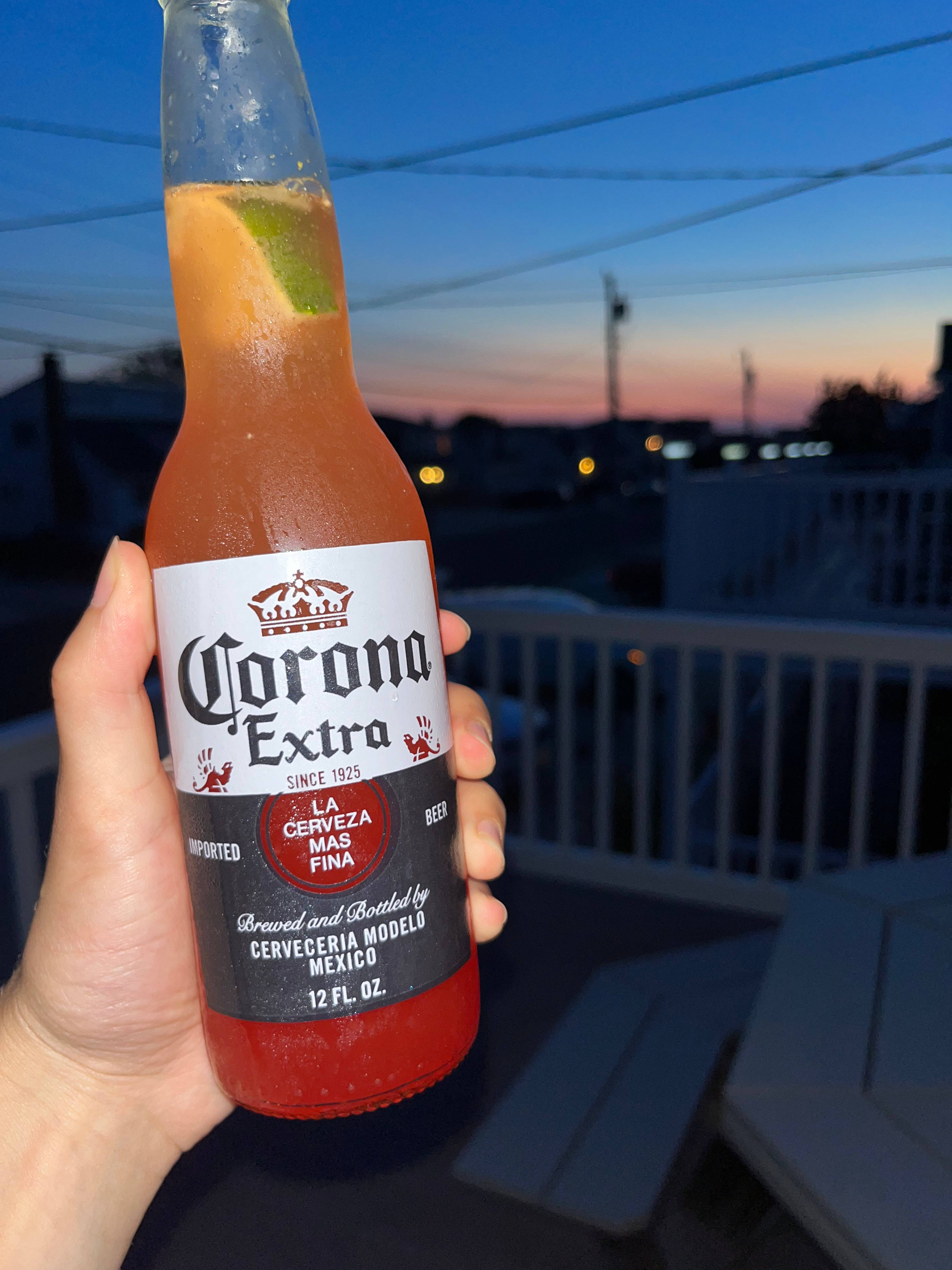 Beer 桌布 壁紙 — 日落時分，一隻手在可俯瞰城市景觀的陽台上拿著一杯加了青檸的冰凍Corona Extra啤酒。
