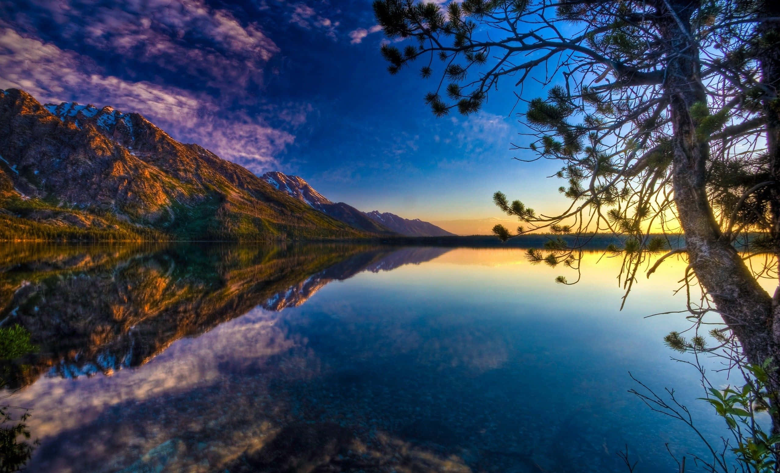 Beautiful Lake 桌布 壁紙 — 日落時分，寧靜的山間湖泊映照出充滿活力的紫色和金色天空，松樹枝條框住了景色。