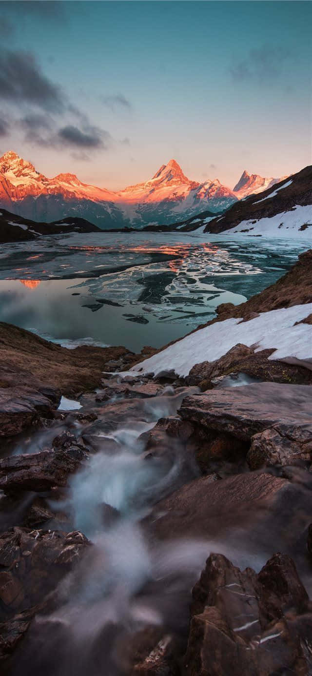瑞士 桌布 壁紙 — 日落時分，寧靜的高山湖泊倒映著積雪的山峰，前景中湍急的溪流流過深色的岩石。