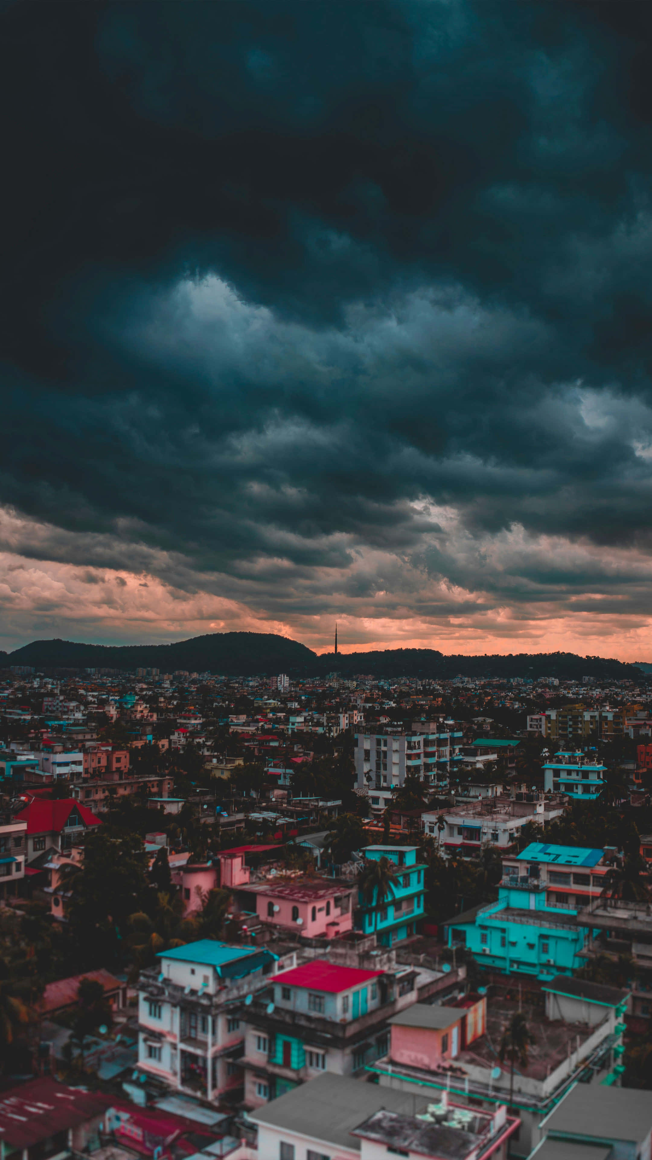 Clouds Aesthetics 桌布 壁紙 — 日落時分，戲劇性的暴風雲層籠罩著色彩繽紛屋頂的密集城市擴張區。
