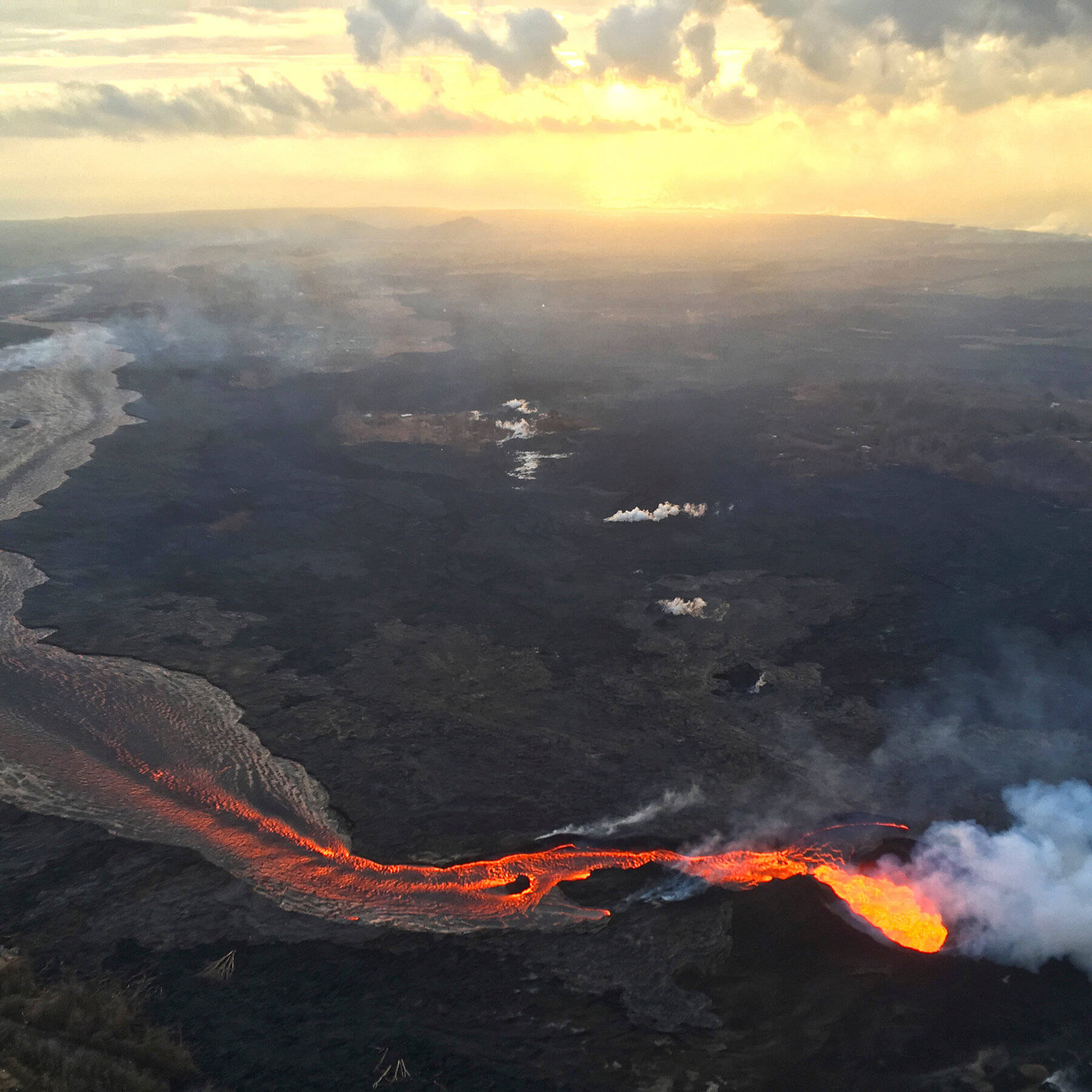 Volcano 桌布 壁紙 — 日落時分，戲劇性的雲層下，發光熔岩流經崎嶇火山地形的鳥瞰圖。