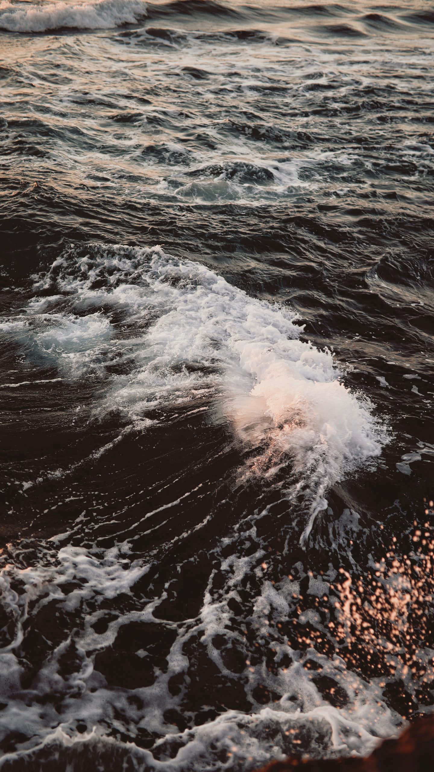 Ocean Aesthetic Phone 桌布 壁紙 — 日落時分，海浪帶著白色泡沫拍打著深色海水，反射出金色的光芒。