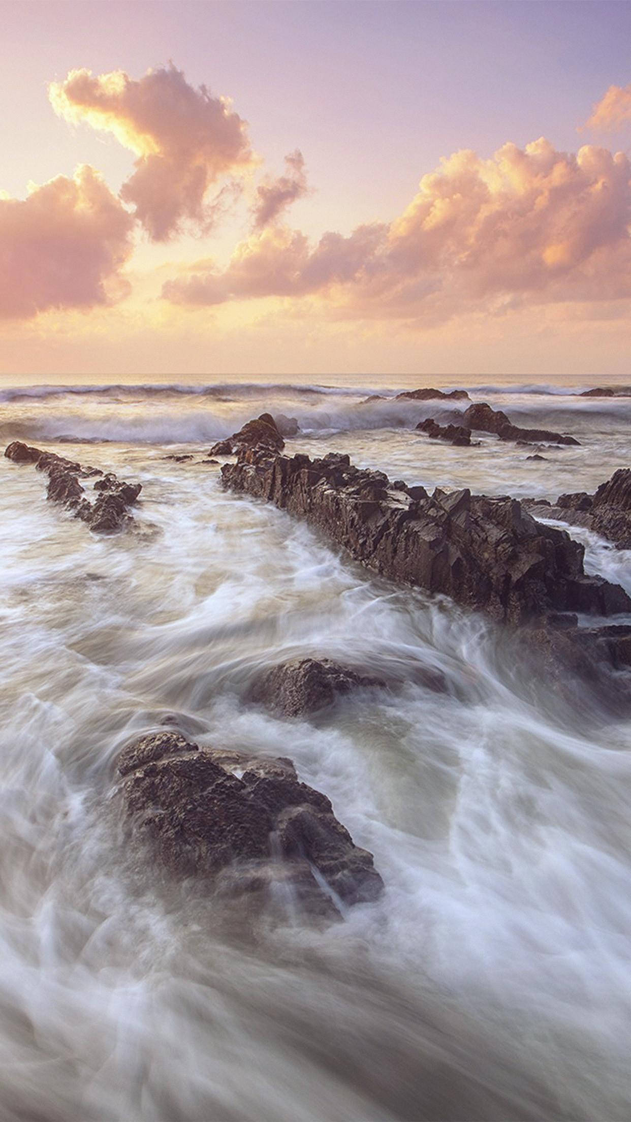 Water Aesthetic 桌布 壁紙 — 日落時分，海浪拍打崎嶇岩石，天空飄著柔和粉紅與橙色雲彩。
