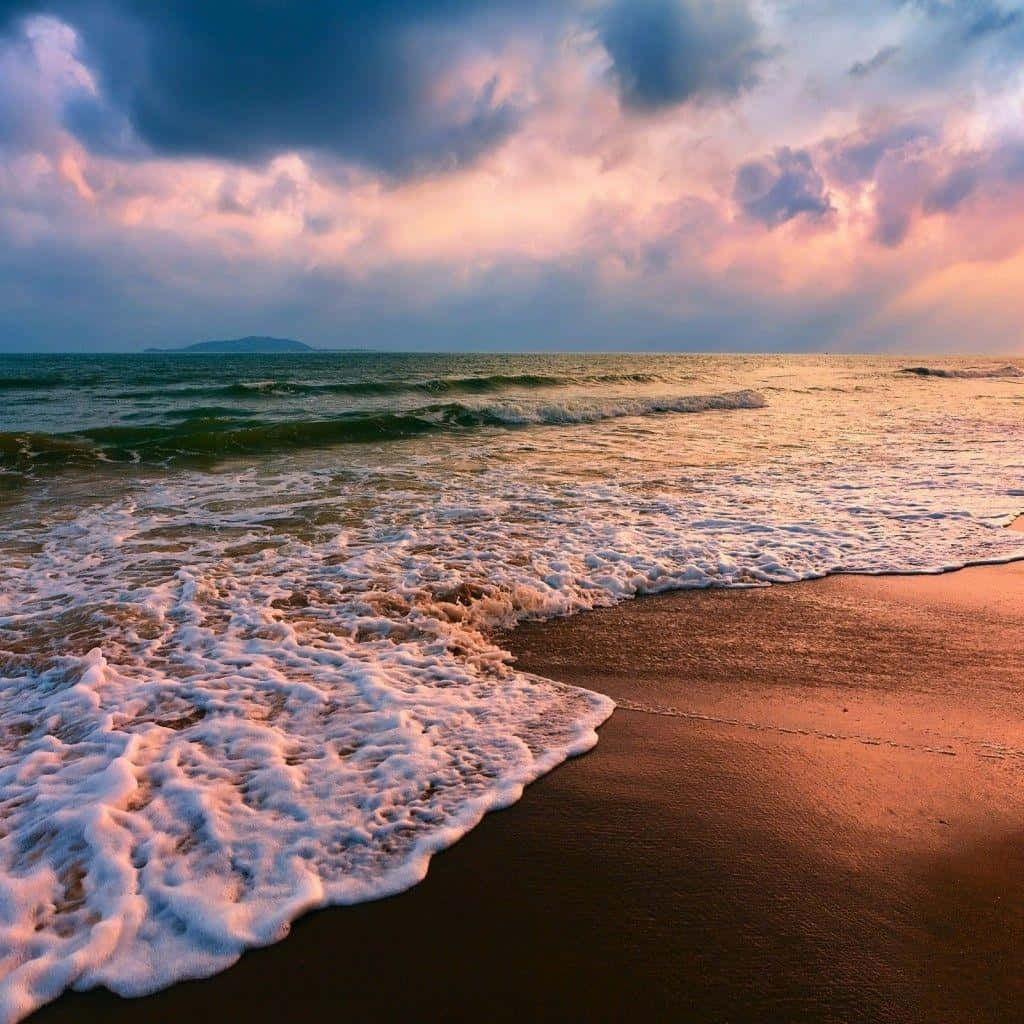 海灘 桌布 壁紙 — 日落時分，海浪拍打沙灘，天空佈滿戲劇性的粉紅與紫色雲彩。
