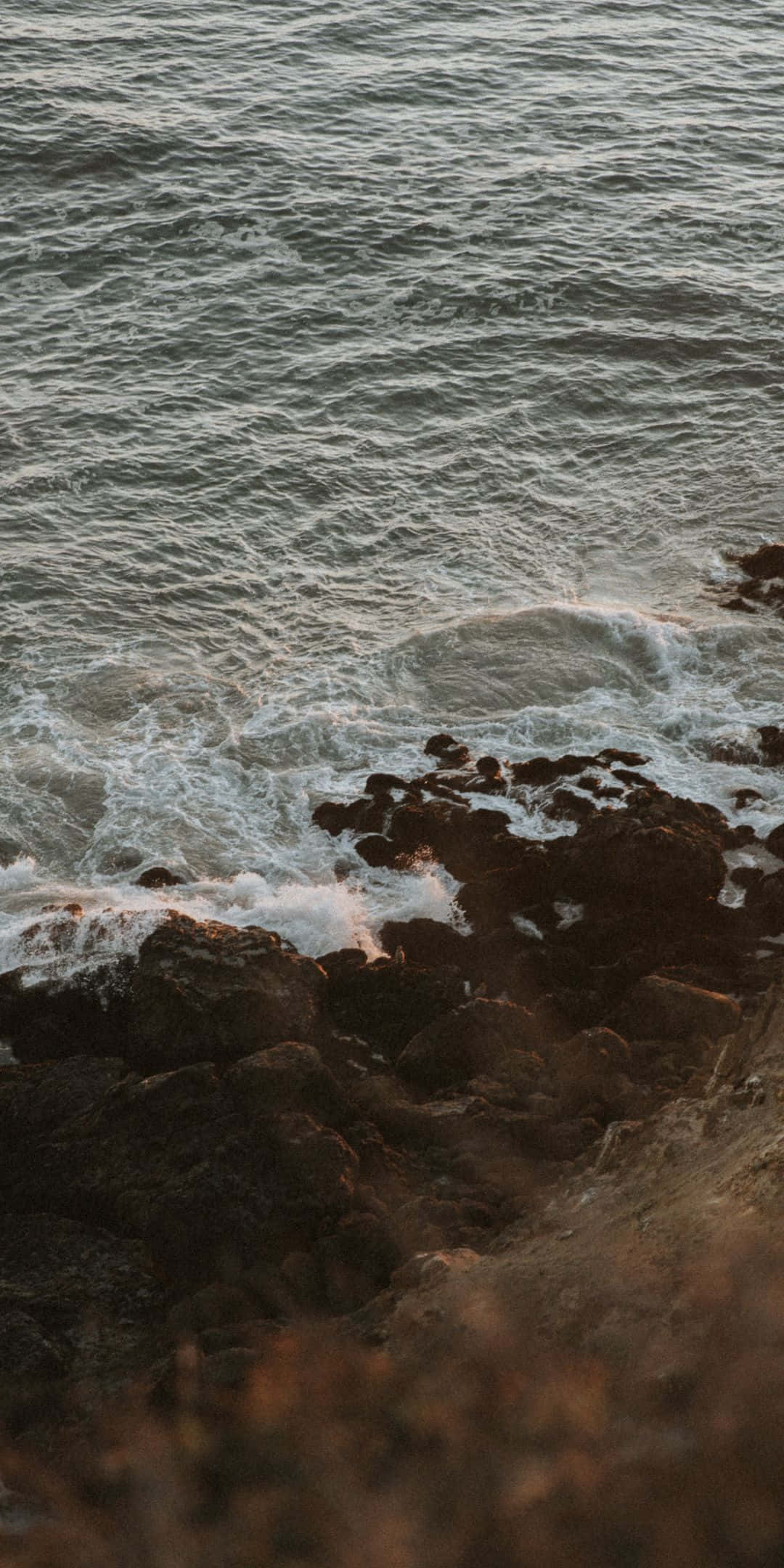 Pixel 3 Malibu 桌布 壁紙 — 日落時分，海浪拍打著暗黑的岩石，在泡沫翻騰的浪花上灑下溫暖的金色光芒。