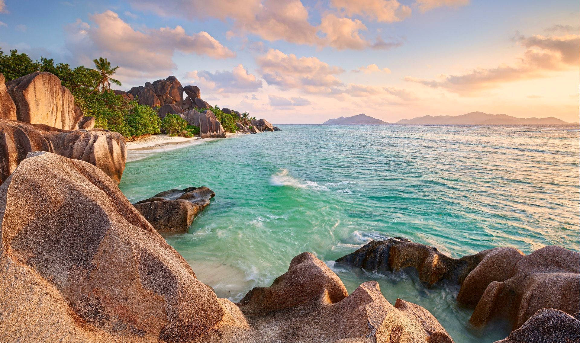 Seychelles 桌布 壁紙 — 日落時分，碧綠的海水和巨大的花崗岩巨石沐浴在陽光下，棕櫚樹點綴在隱秘的熱帶海灘上。