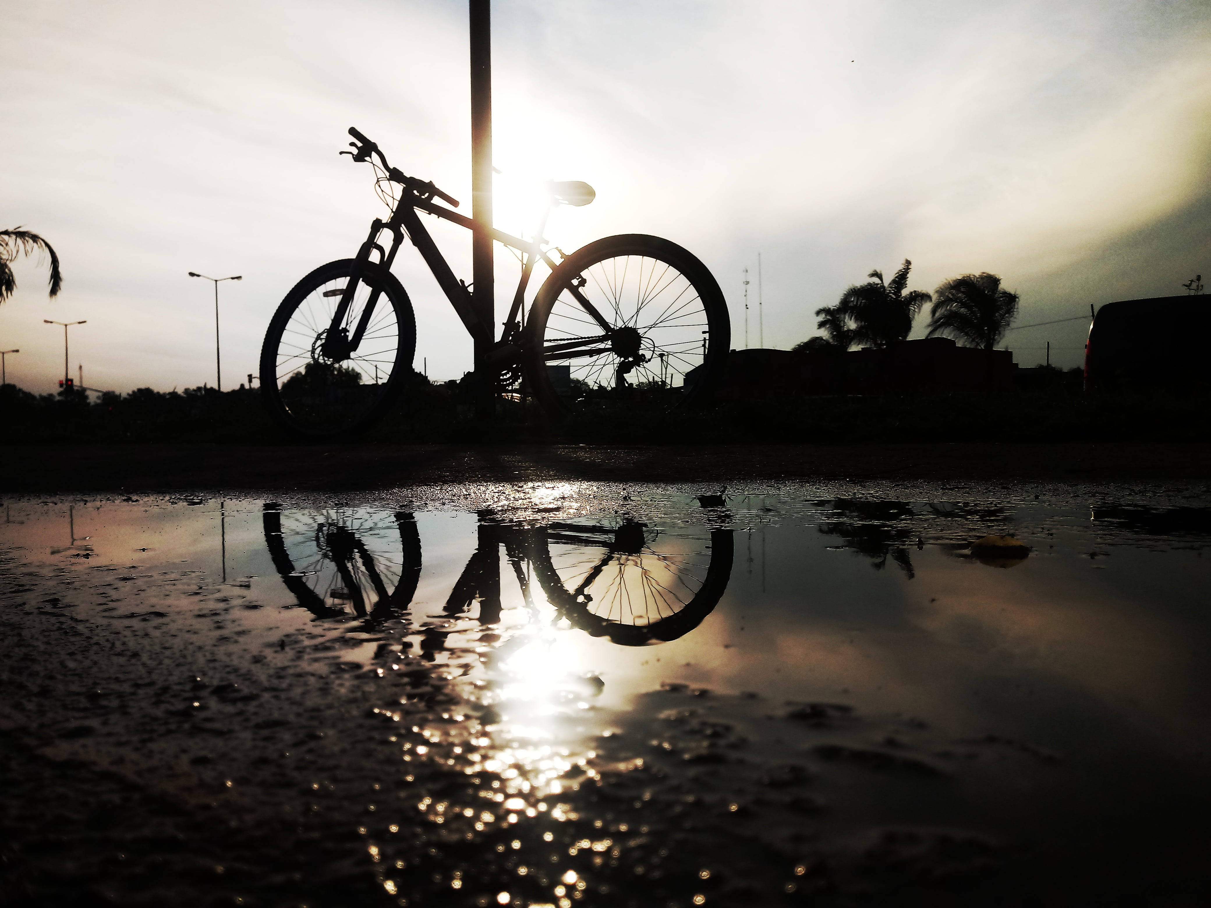 Mountain Bike 桌布 壁紙 — 日落時分，腳踏車靠著柱子的剪影倒映在雨水坑中。