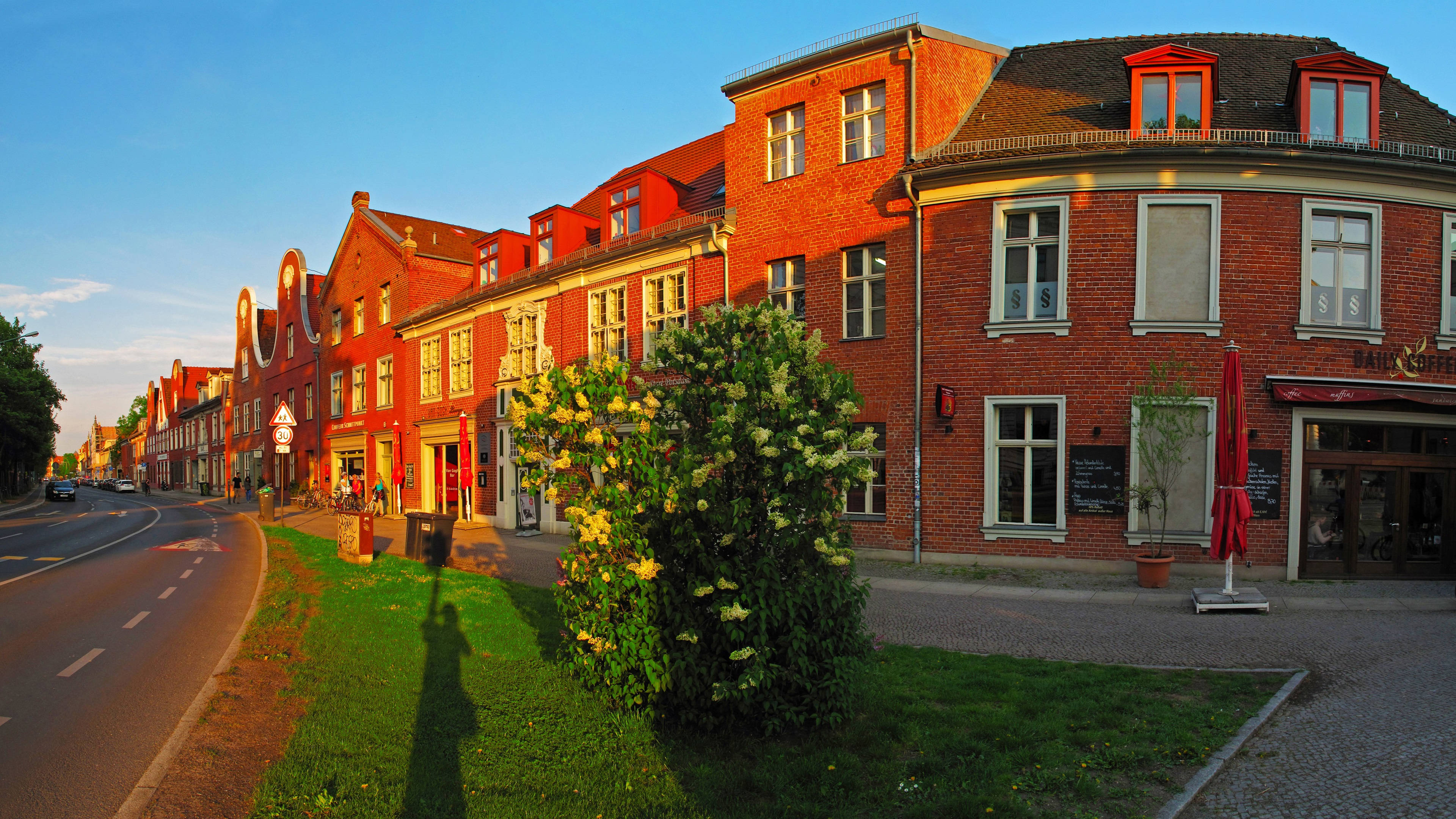 Potsdam 桌布 壁紙 — 日落時分，金色暖光灑在寧靜的歐洲街道上，映照著紅磚建築和盛開的繡球花。