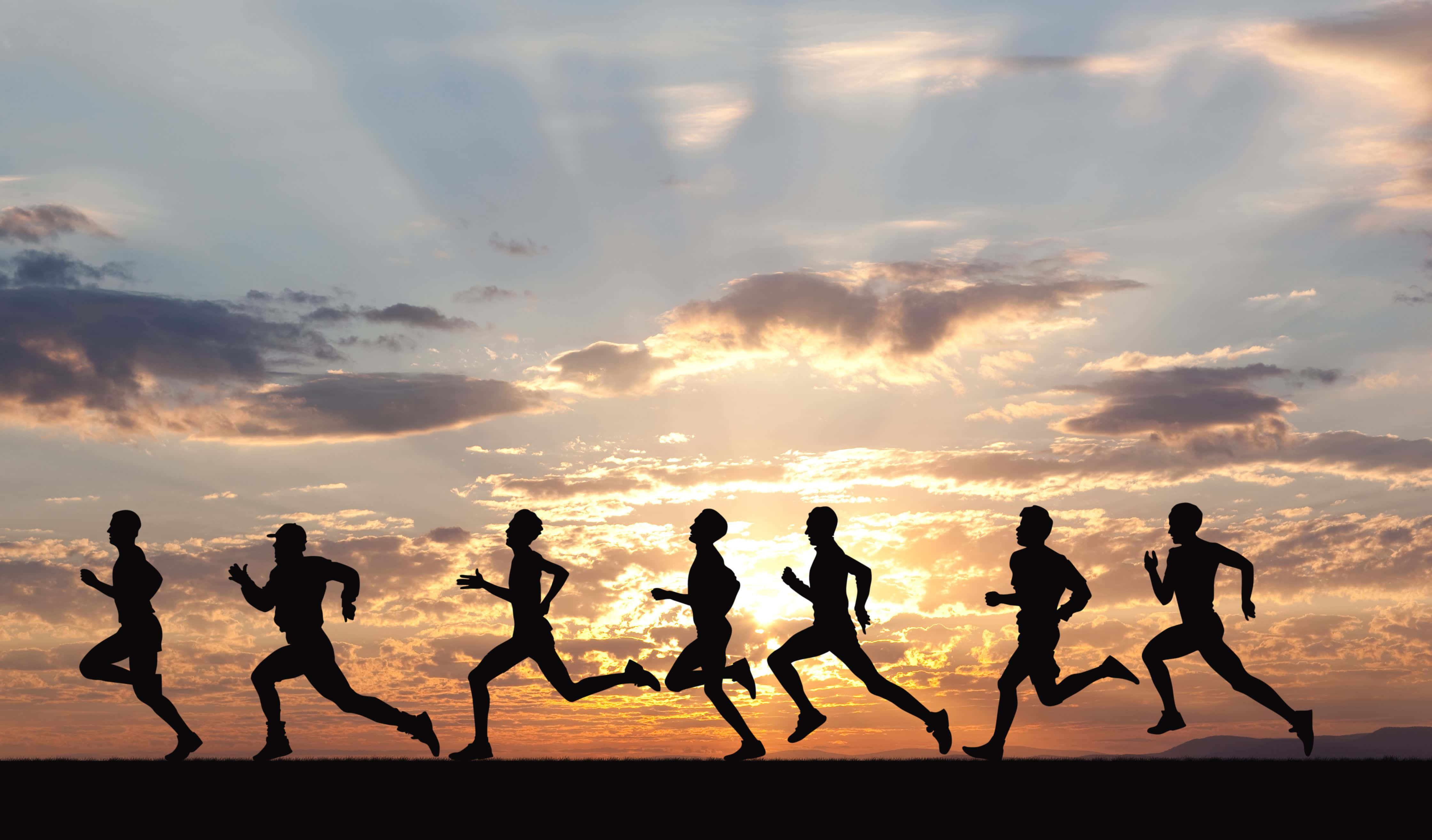 Running 桌布 壁紙 — 日落時分，金色雲彩和燦爛陽光下，跑步者的剪影在地平線上飛奔。