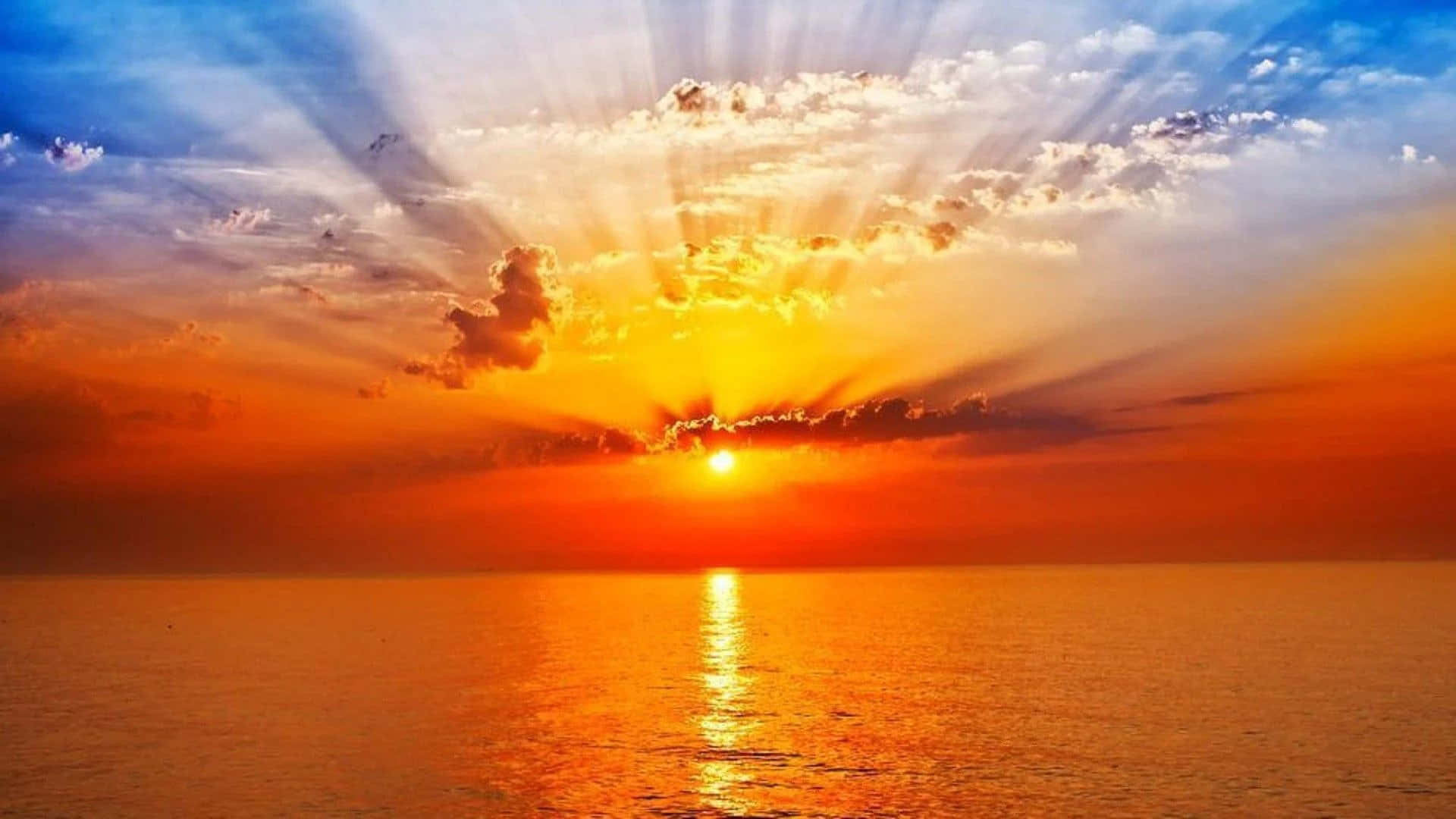 海洋 桌布 壁紙 — 日落時分，陽光穿透雲層，照射在平靜的海面上，在水面映出金色倒影。