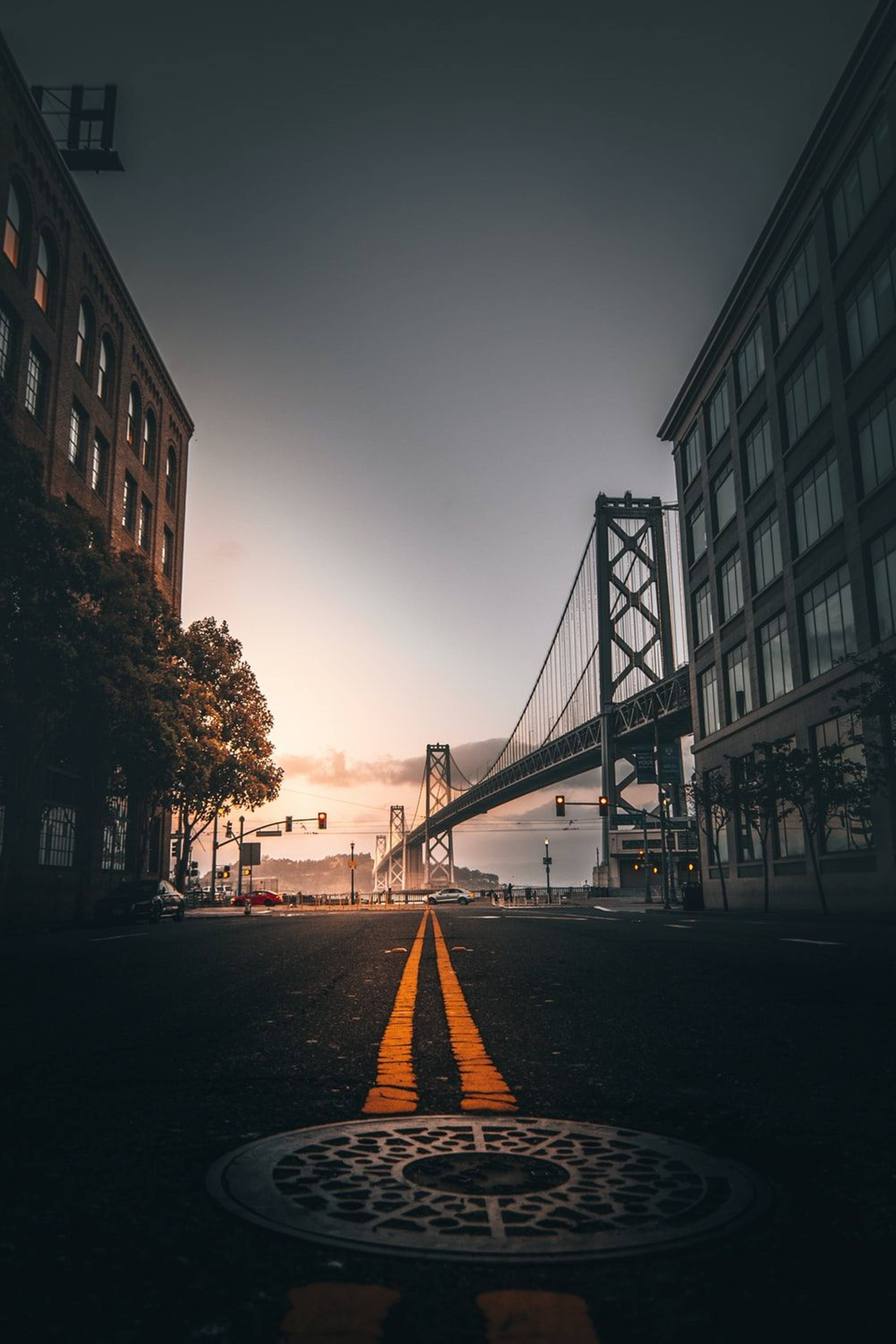 san francisco iPhone 桌布 壁紙 — 日落時分低角度城市街景，橋樑延伸至遠方，兩旁高樓大廈環繞。