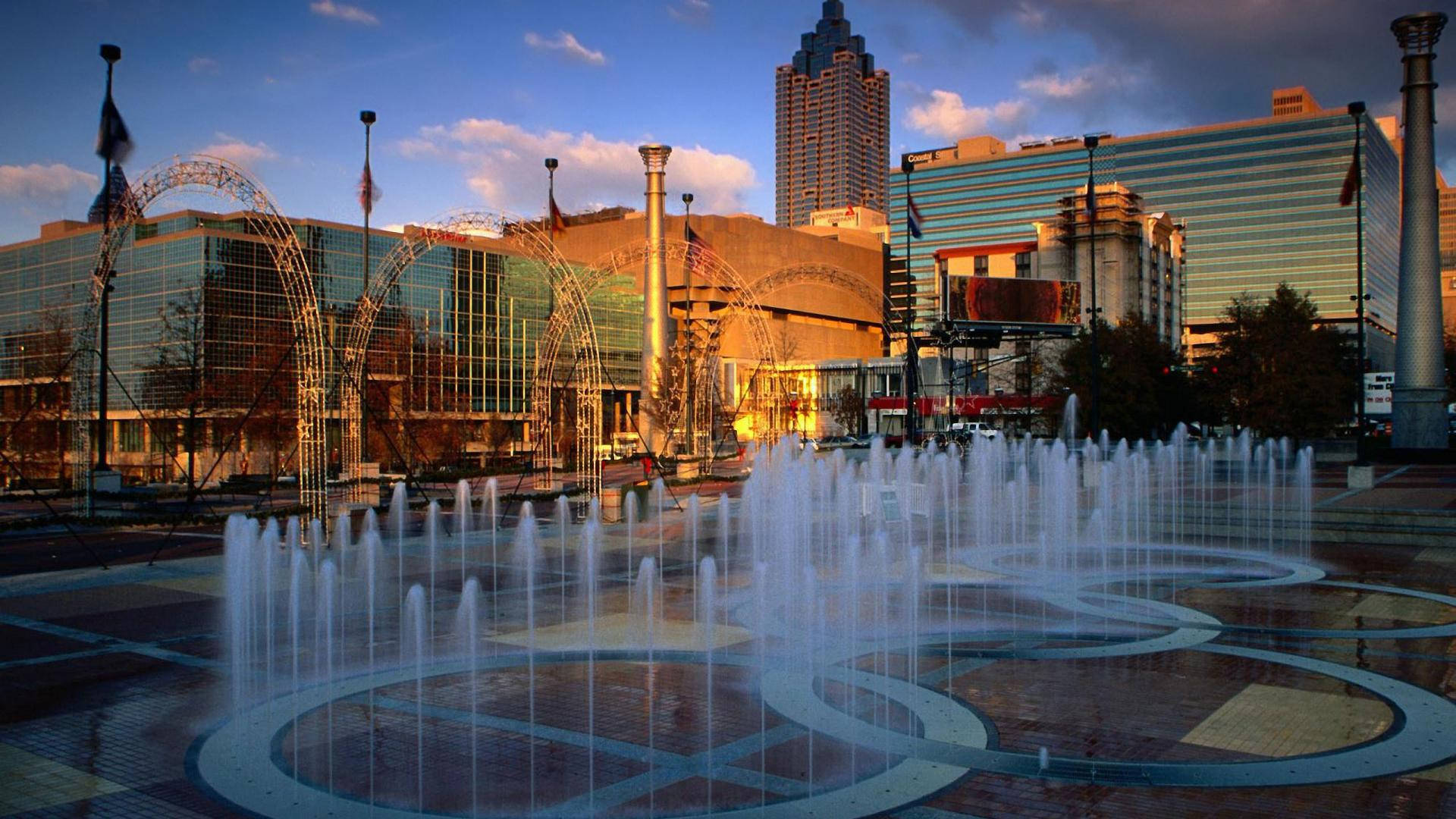 Atlanta 桌布 壁紙 — 日落時分充滿活力的城市廣場，設有動態噴泉，弧形水柱和現代玻璃建築反射著金色的光芒。