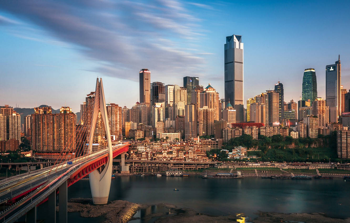 Chongqing 桌布 壁紙 — 日落時分充滿活力的城市景觀，一座醒目的紅色橋樑橫跨河流，高聳的摩天大樓反射著金色的光芒。