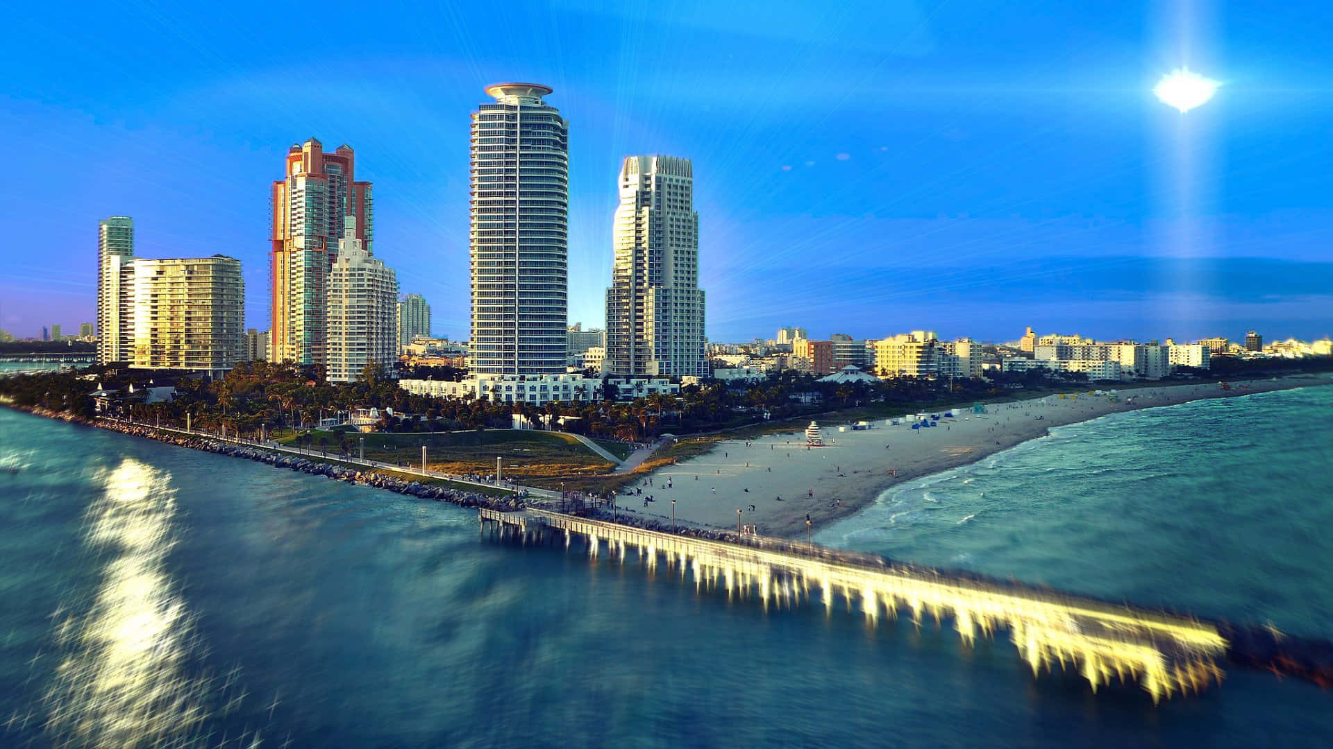 Miami 桌布 壁紙 — 日落時分充滿活力的沿海城市鳥瞰圖，高樓大廈、長長的碼頭和熙熙攘攘的海灘，天空湛藍明亮。