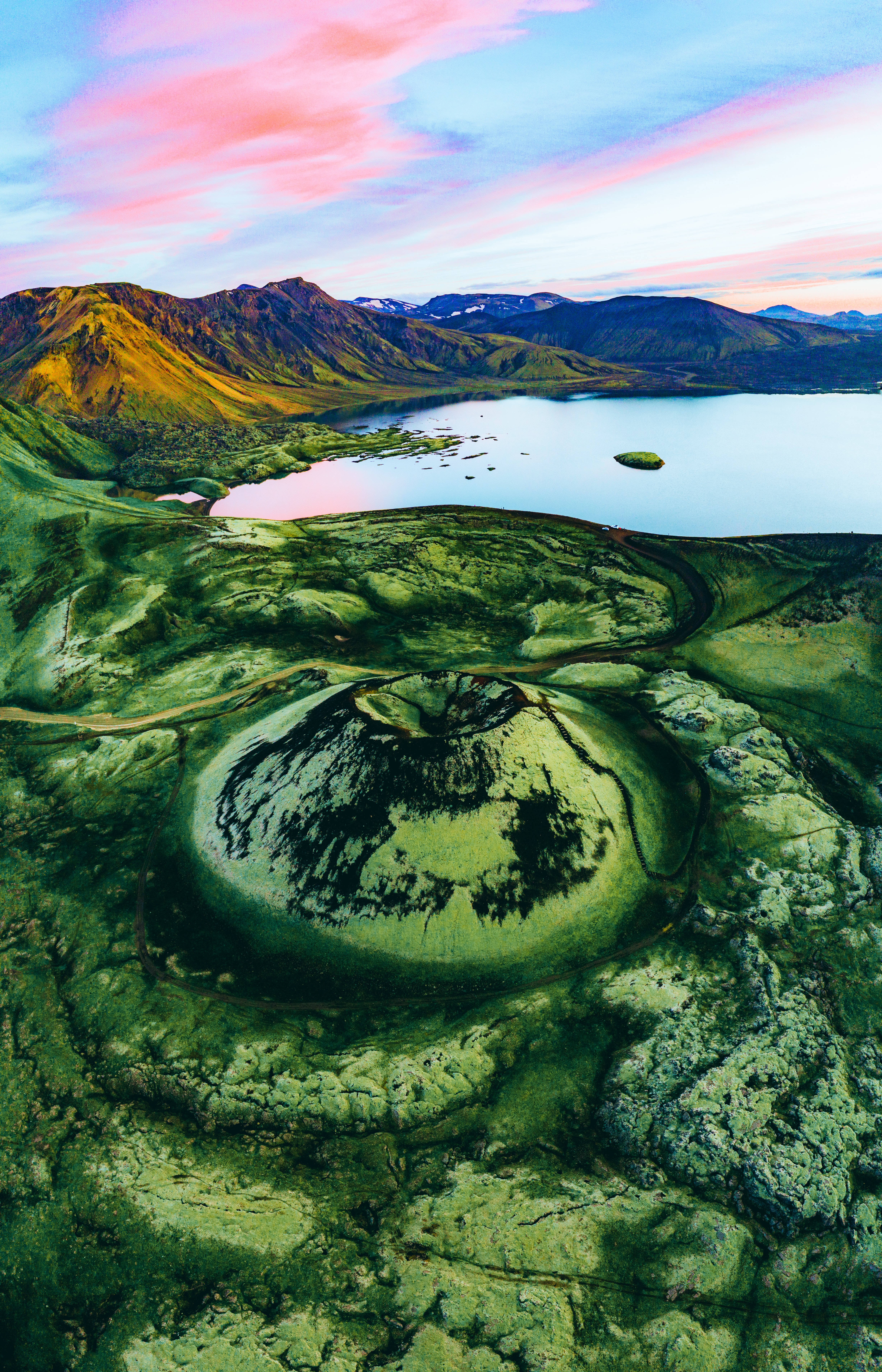 冰島 桌布 壁紙 — 日落時分充滿活力的綠色火山口湖的鳥瞰圖，背景是粉紅色和藍色的天空山脈。