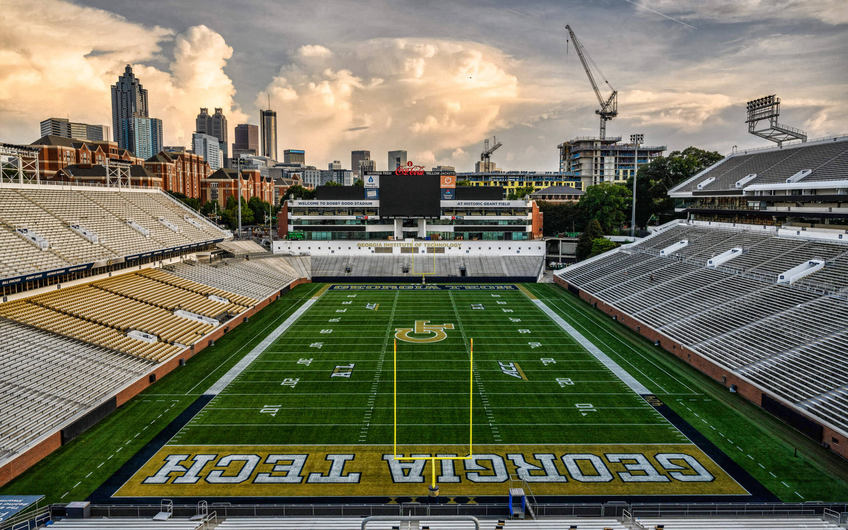 Football Field 桌布 壁紙 — 日落時分喬治亞理工學院空無一人的足球場鳥瞰圖，背景有城市天際線和建築起重機。