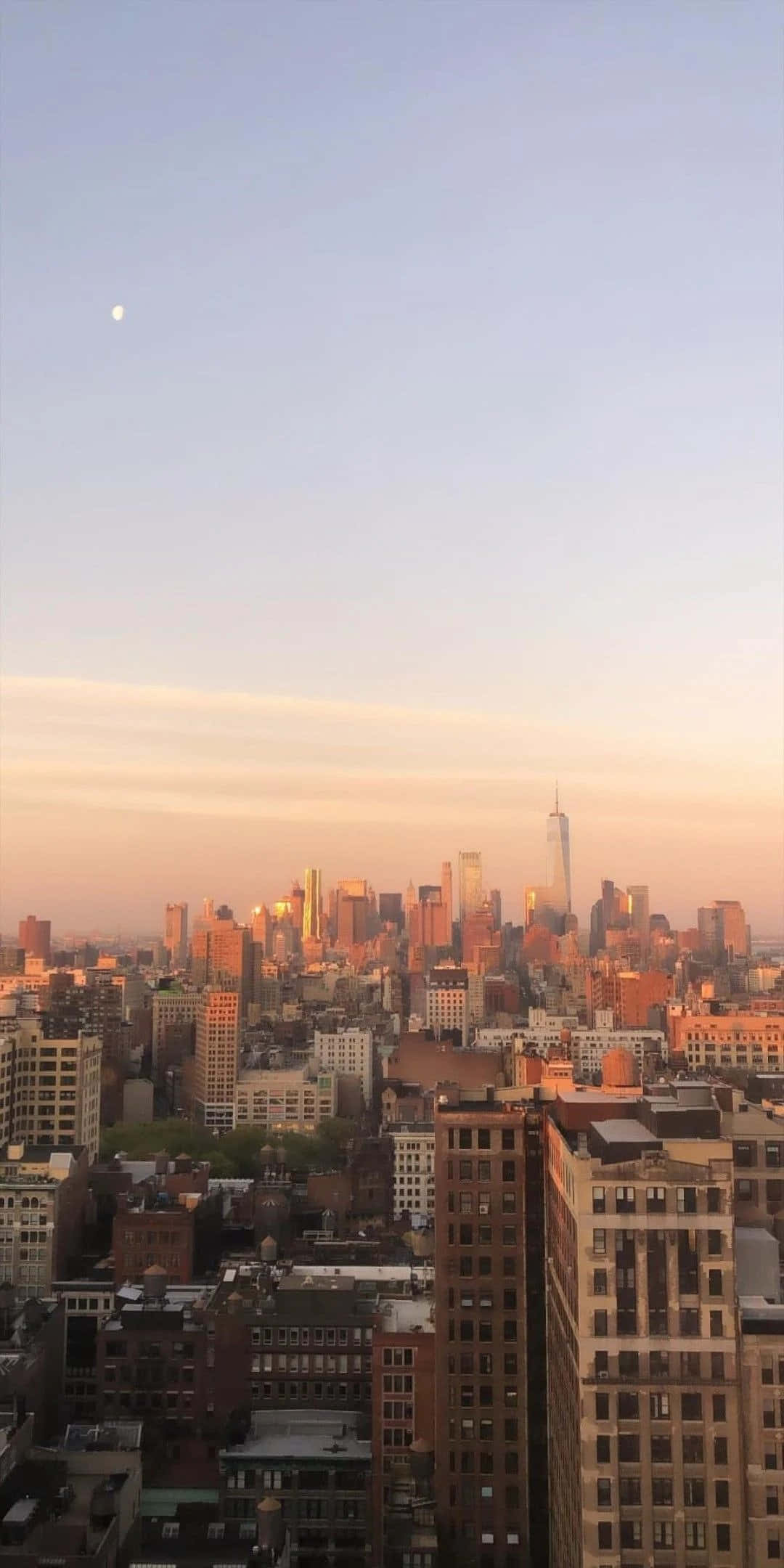 Nyc Aesthetic 桌布 壁紙 — 日落時分城市天際線的全景視圖，溫暖的金色光芒沐浴著摩天大樓，蒼白的天空中可見一彎新月。
