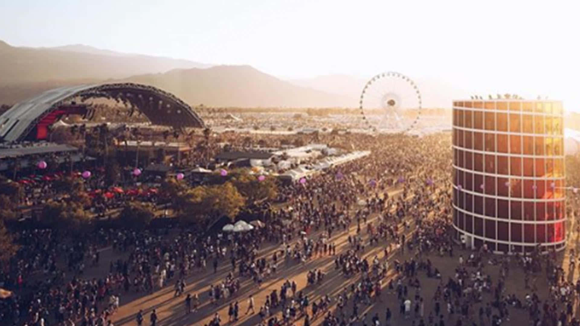 Coachella 桌布 壁紙 — 日落時分大型戶外音樂節的鳥瞰圖，人群、舞台、摩天輪和背景中的山脈。