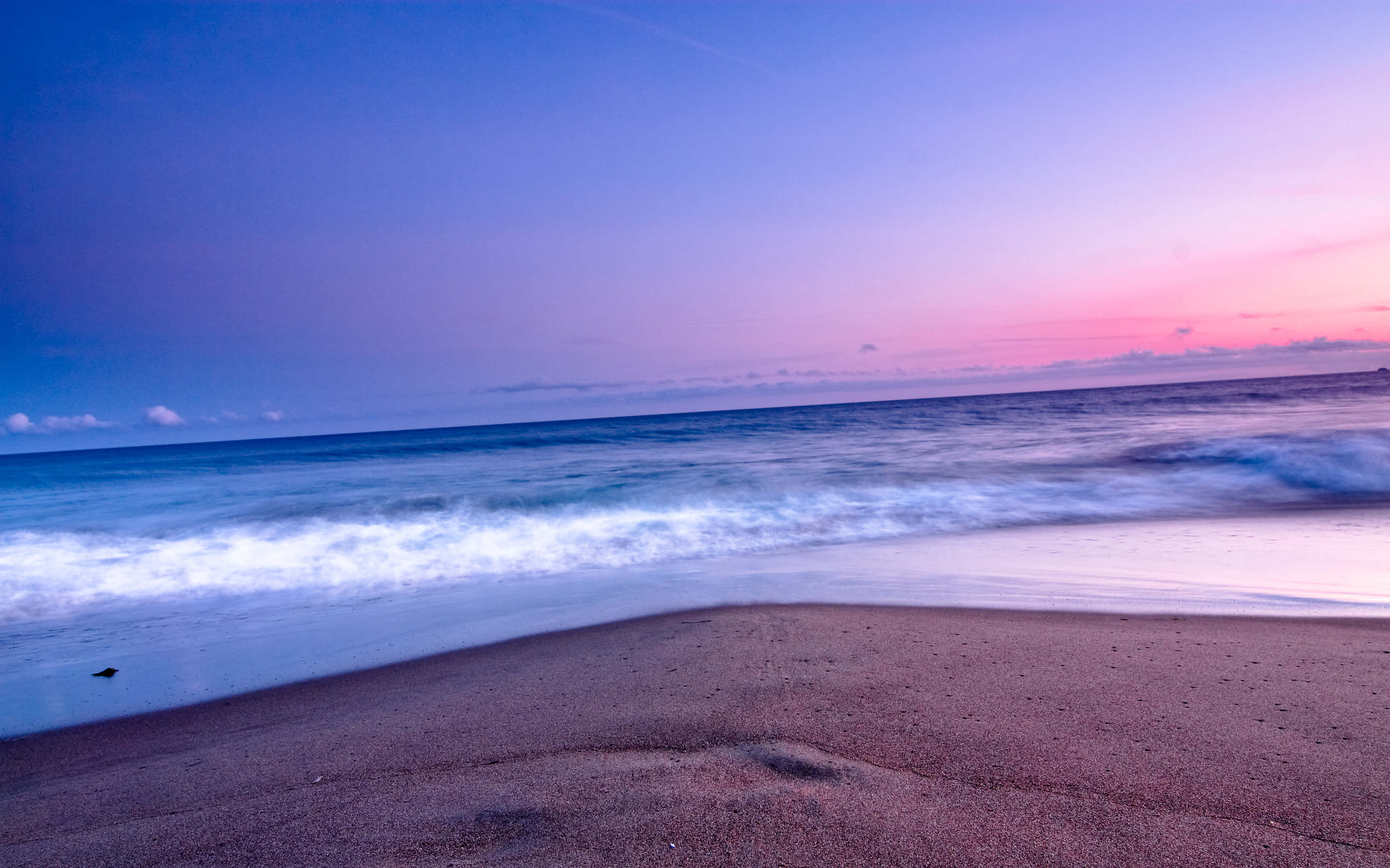 Beautiful Ocean 桌布 壁紙 — 日落時分寧靜的海灘，柔和的粉紅與藍色天空映照在輕柔拍打沙岸的波浪上。