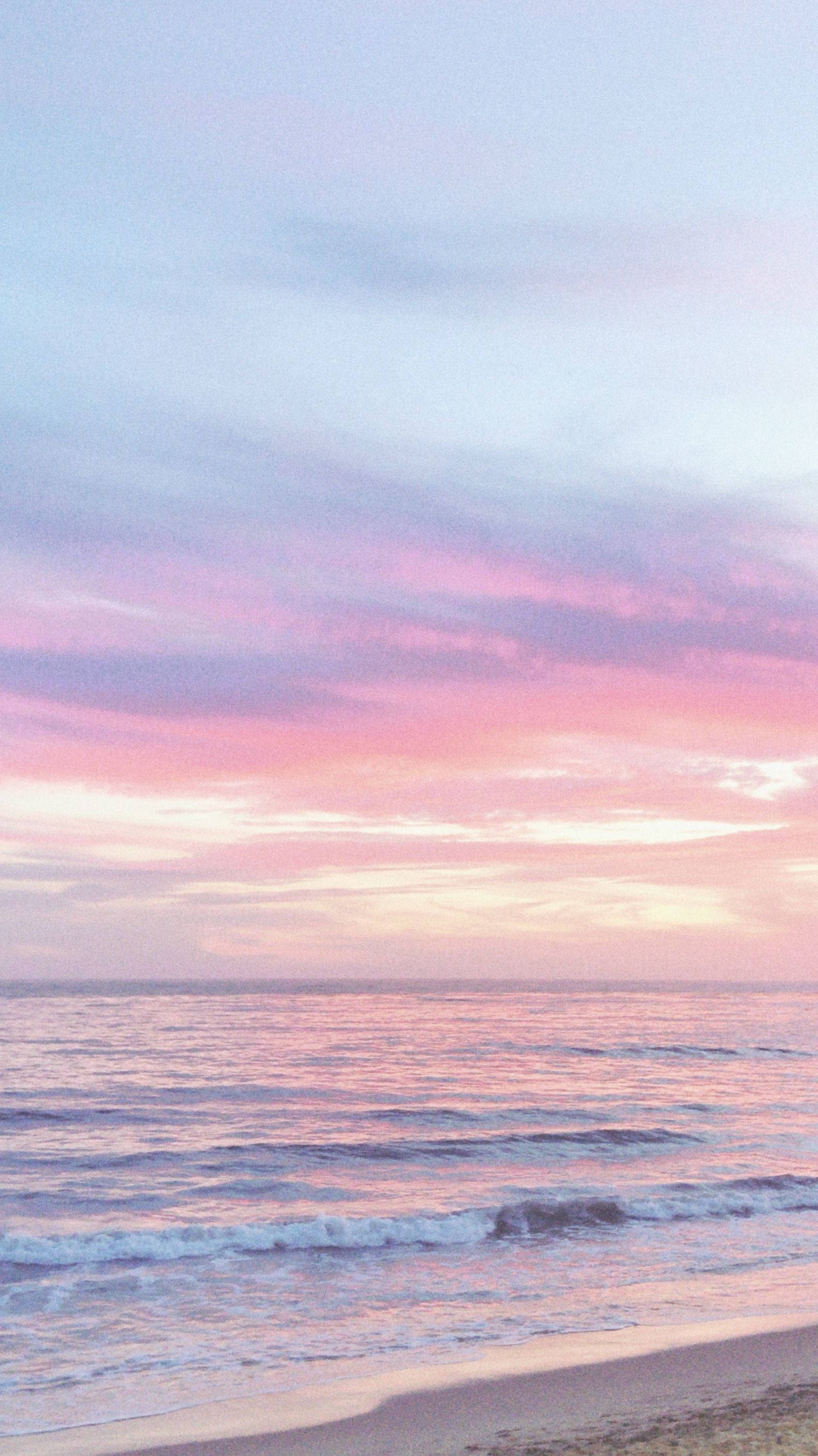 Aesthetic Sunset 桌布 壁紙 — 日落時分寧靜的海灘，柔和的粉紅色和薰衣草色雲彩映照在溫柔的海浪上。