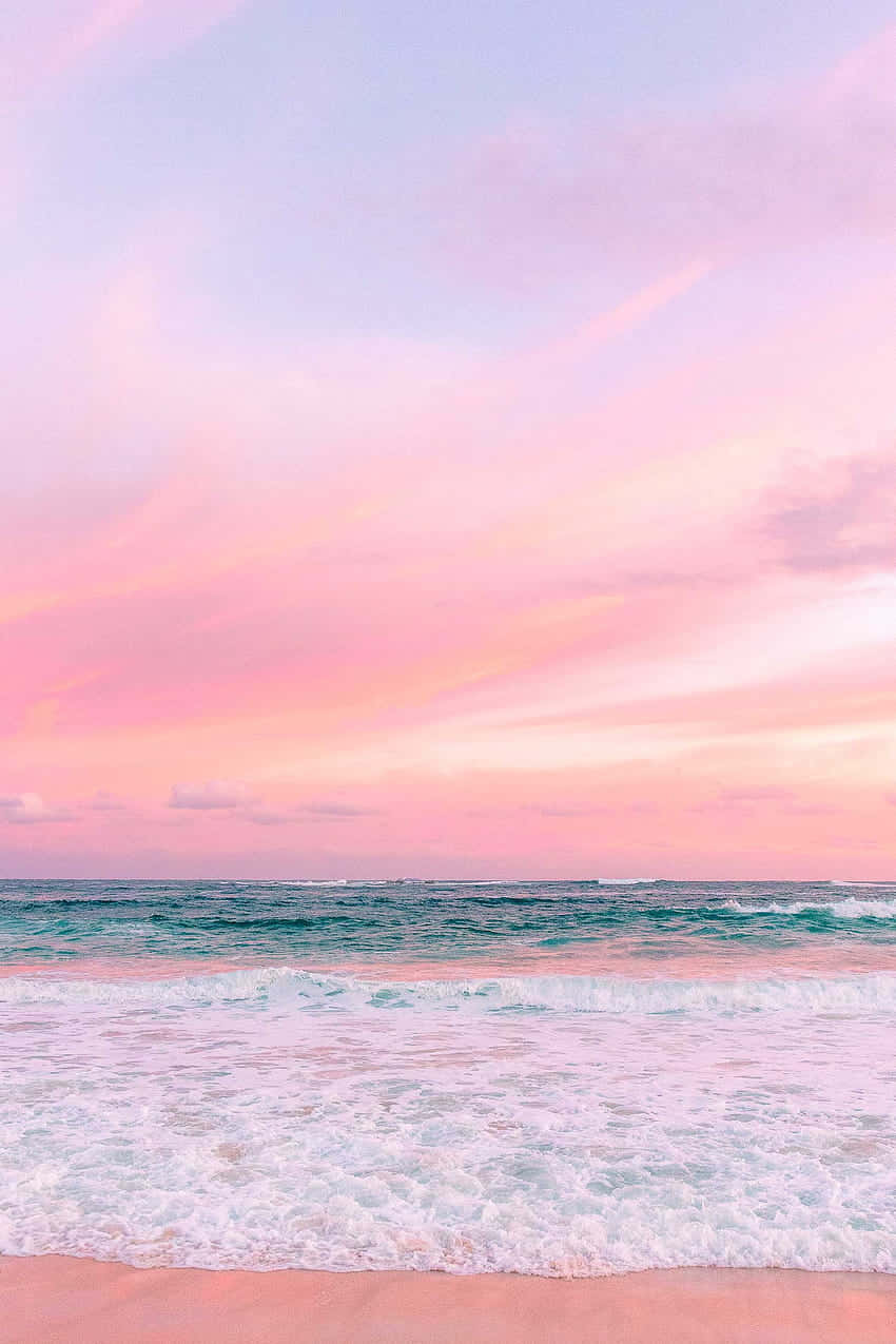 Pastel Beach 桌布 壁紙 — 日落時分寧靜的海灘，粉紅色的天空映照在碧綠色的海浪和粉紅色的沙灘上。