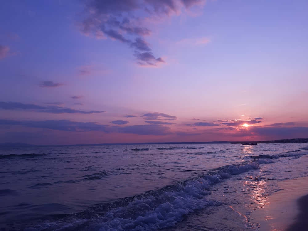 Sunset Beach 桌布 壁紙 — 日落時分寧靜的海灘，紫色和粉紅色的天空倒映在輕柔的海浪上，拍打著濕沙。