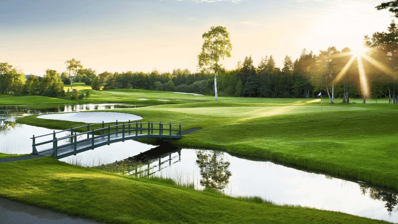 720p Golf Course 桌布 壁紙 — 日落時分寧靜的高爾夫球場，一座木橋橫跨平靜的水障礙，周圍環繞著鬱鬱蔥蔥的綠色球道和樹木。