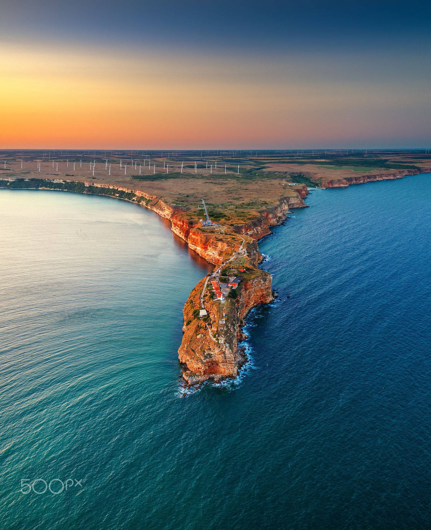 Bulgaria 桌布 壁紙 — 日落時分崎嶇海岸半島的鳥瞰圖，碧綠的海水與遠方海岸點綴的風力發電機。