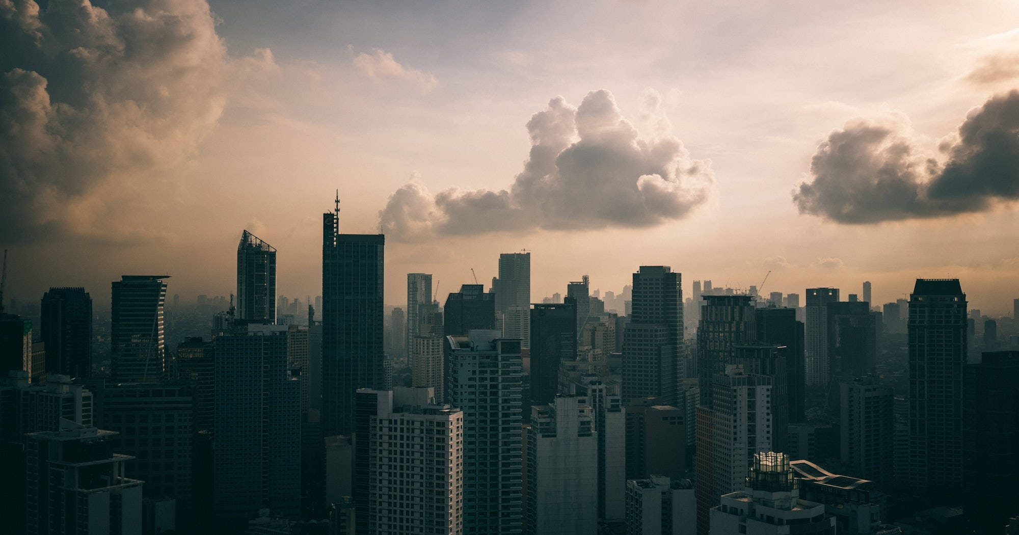 Skyscraper 桌布 壁紙 — 日落時分廣闊的城市天際線，高聳的摩天大樓在溫暖的金色天空襯托下形成剪影，天空點綴著戲劇性的雲彩。