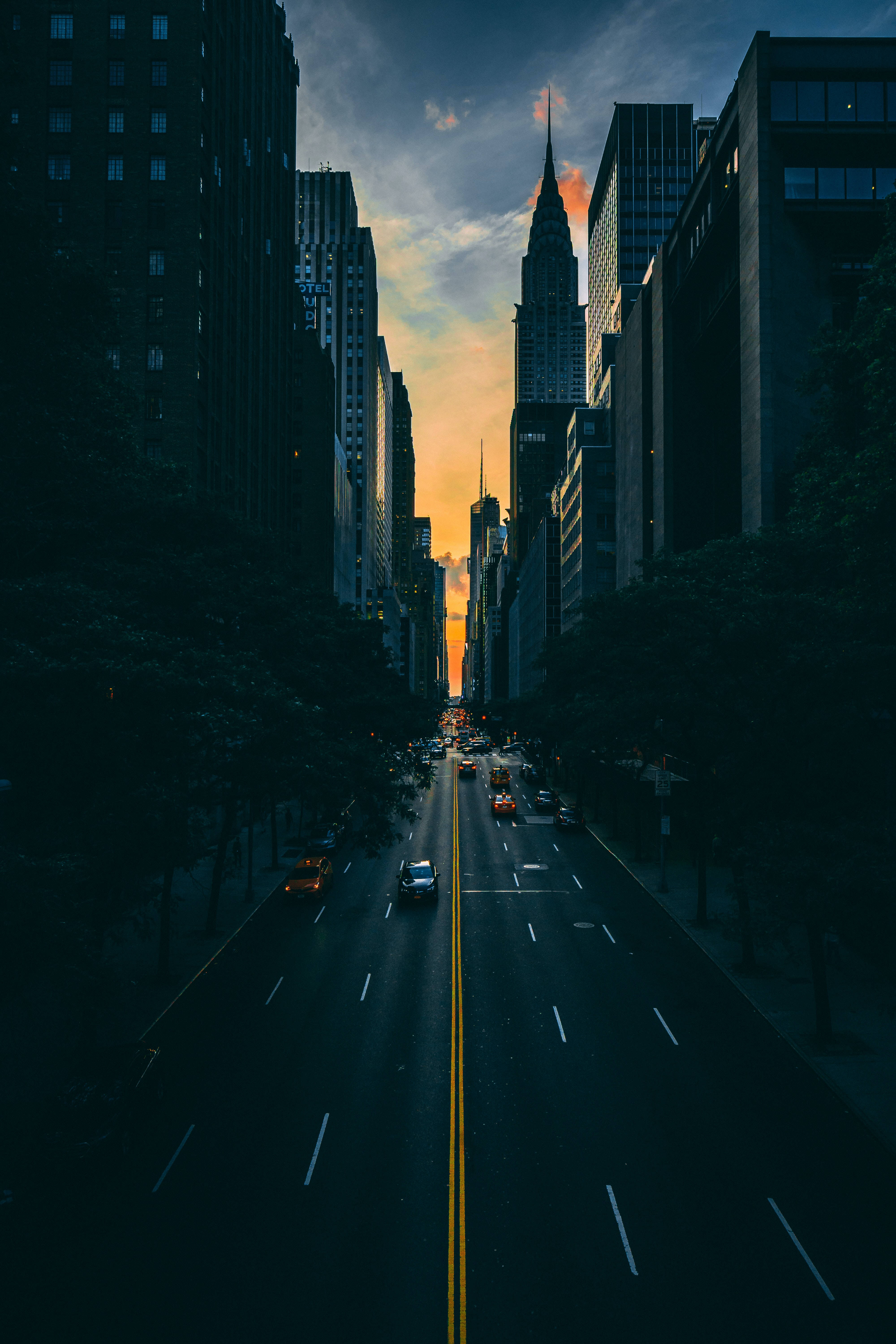 New York 桌布 壁紙 — 日落時分戲劇性的城市峽谷，高聳的摩天大樓框住繁忙街道上方發光的天空。