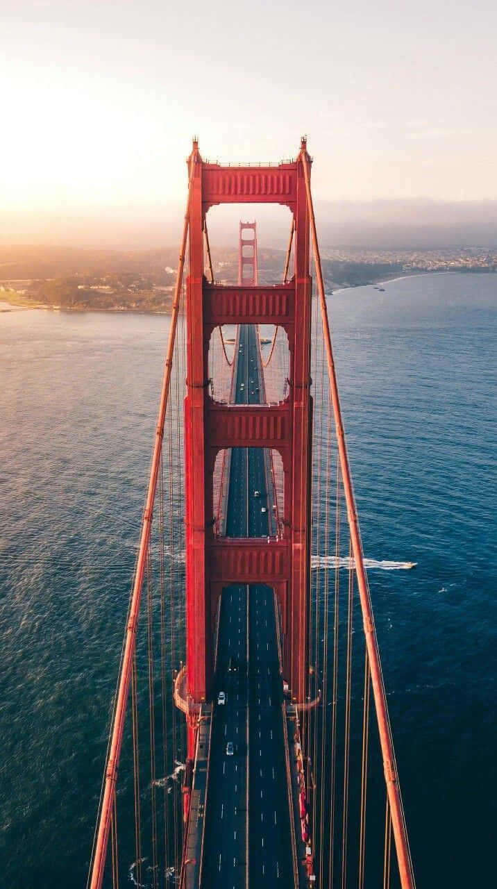 bridge 桌布 壁紙 — 日落時分標誌性的紅色金門大橋的鳥瞰圖，汽車在其跨度上行駛，下方是深藍色的海水。