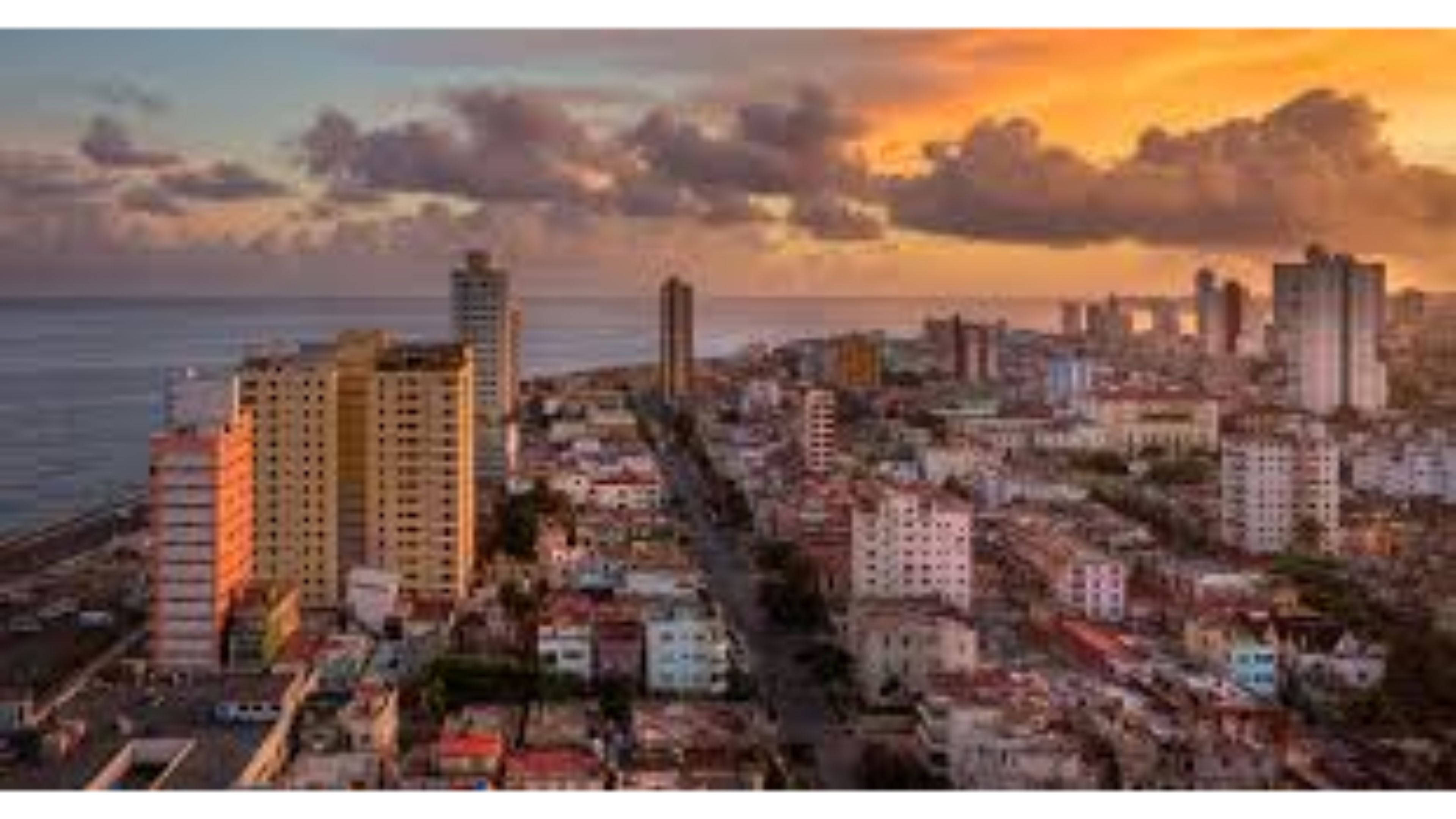 Cuba 桌布 壁紙 — 日落時分沿海城市的鳥瞰圖，溫暖的金色光芒照亮了高層建築和海洋旁密集的城市擴張。