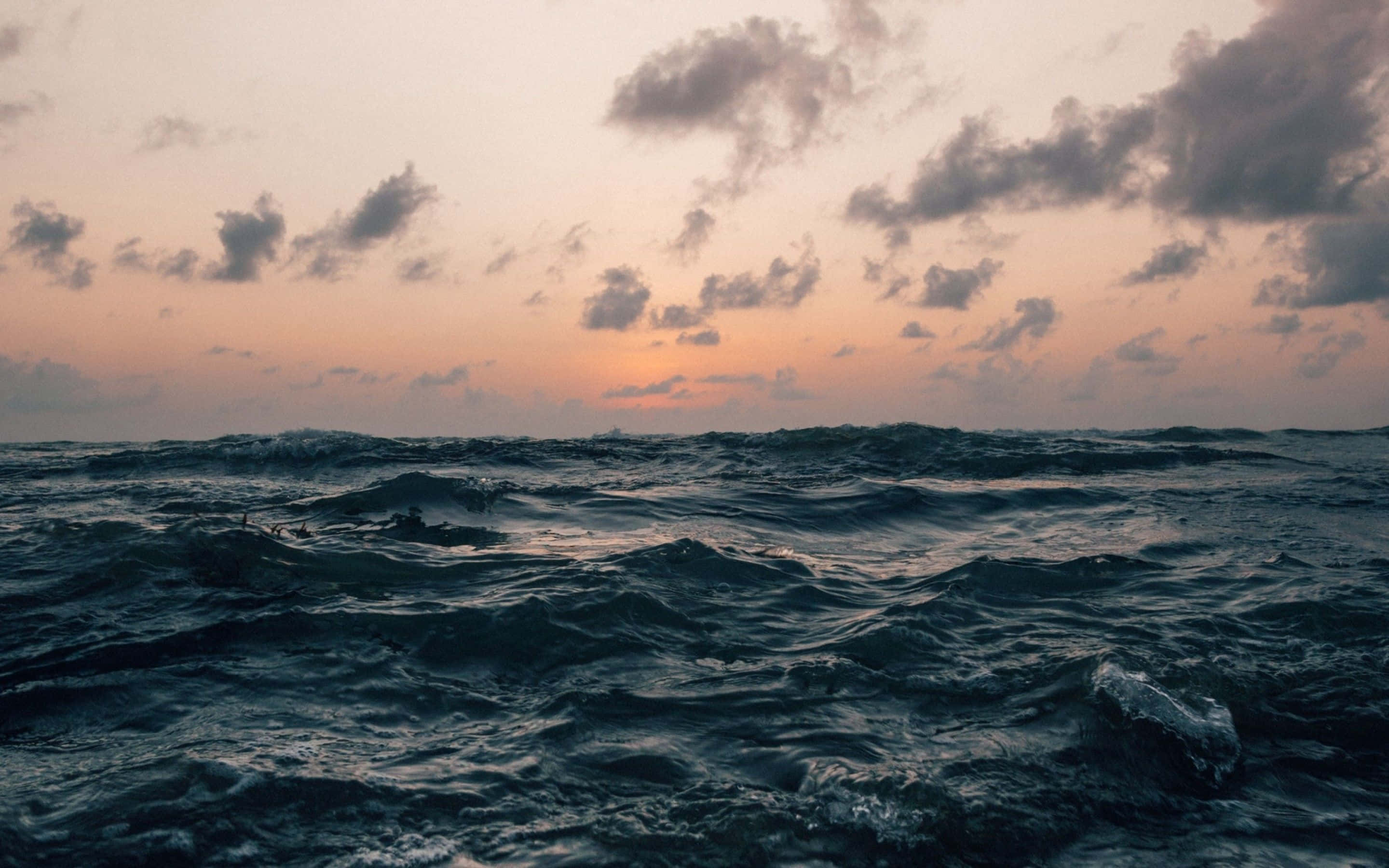 waves 桌布 壁紙 — 日落時分波濤洶湧的海洋，在染上橙黃和粉紅色的多雲天空下，深色波浪翻騰。