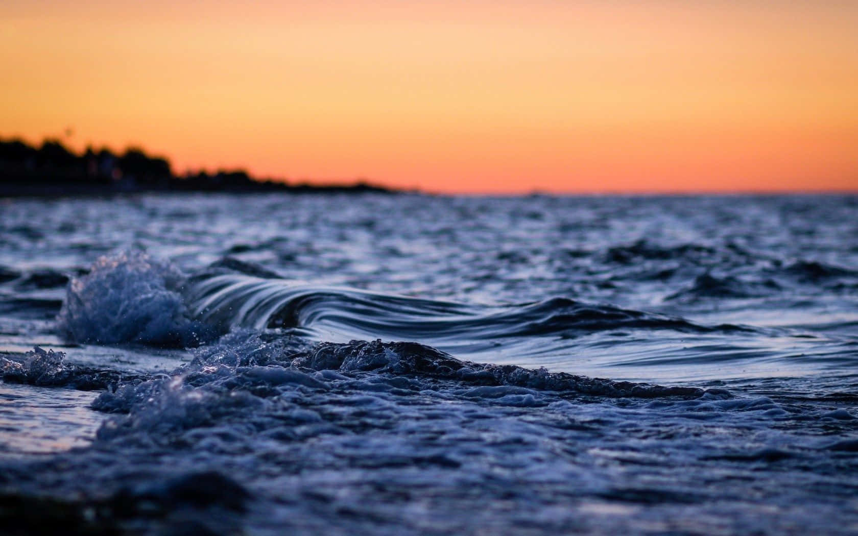 Ocean Waves 桌布 壁紙 — 日落時分海浪拍打的近景，伴隨鮮豔的橙色天空和深藍色海水。