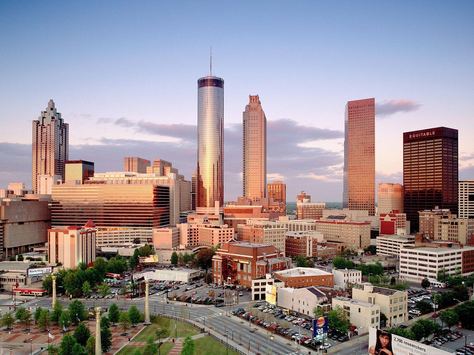 Atlanta 桌布 壁紙 — 日落時分現代城市天際線的全景視圖，高聳的玻璃摩天大樓在柔和的藍天下反射出溫暖的金色光芒。