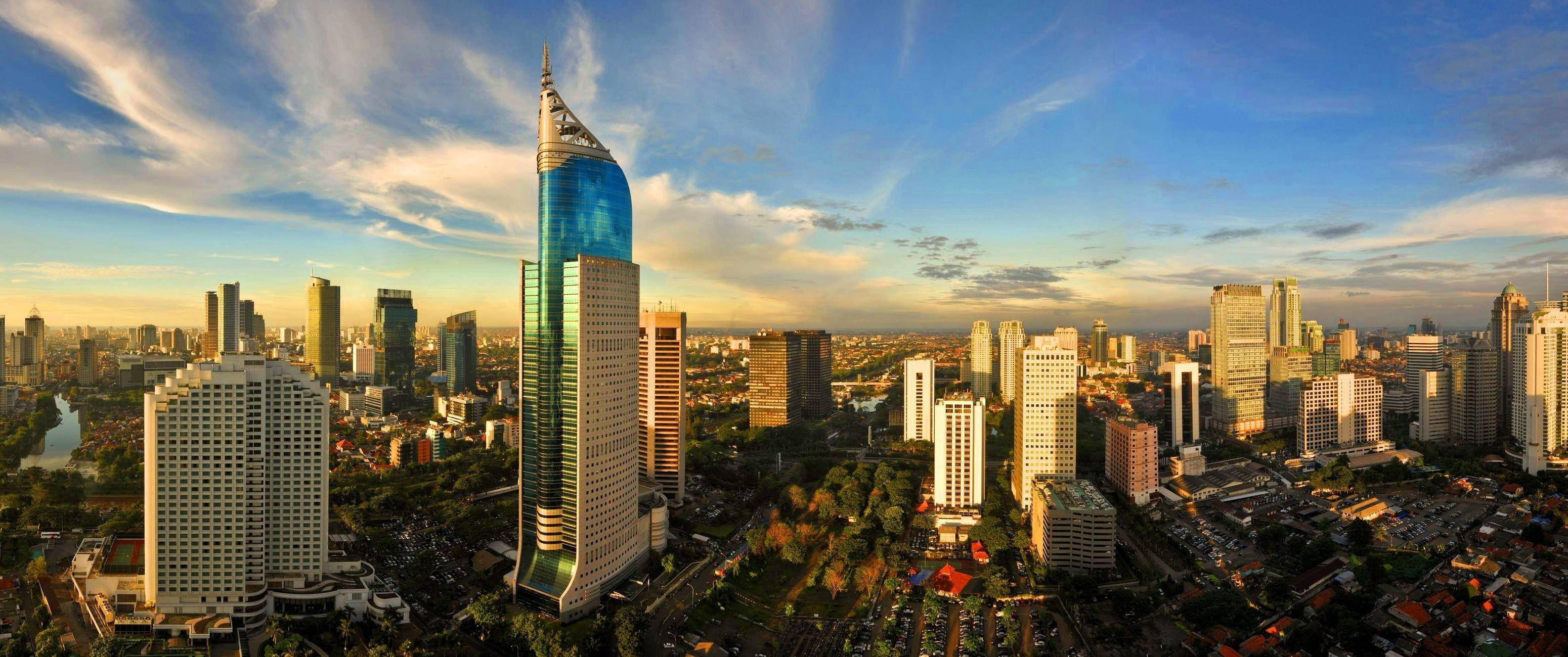 Jakarta 桌布 壁紙 — 日落時分現代城市景觀的鳥瞰圖，一座引人注目的藍色玻璃摩天大樓主導著天際線。