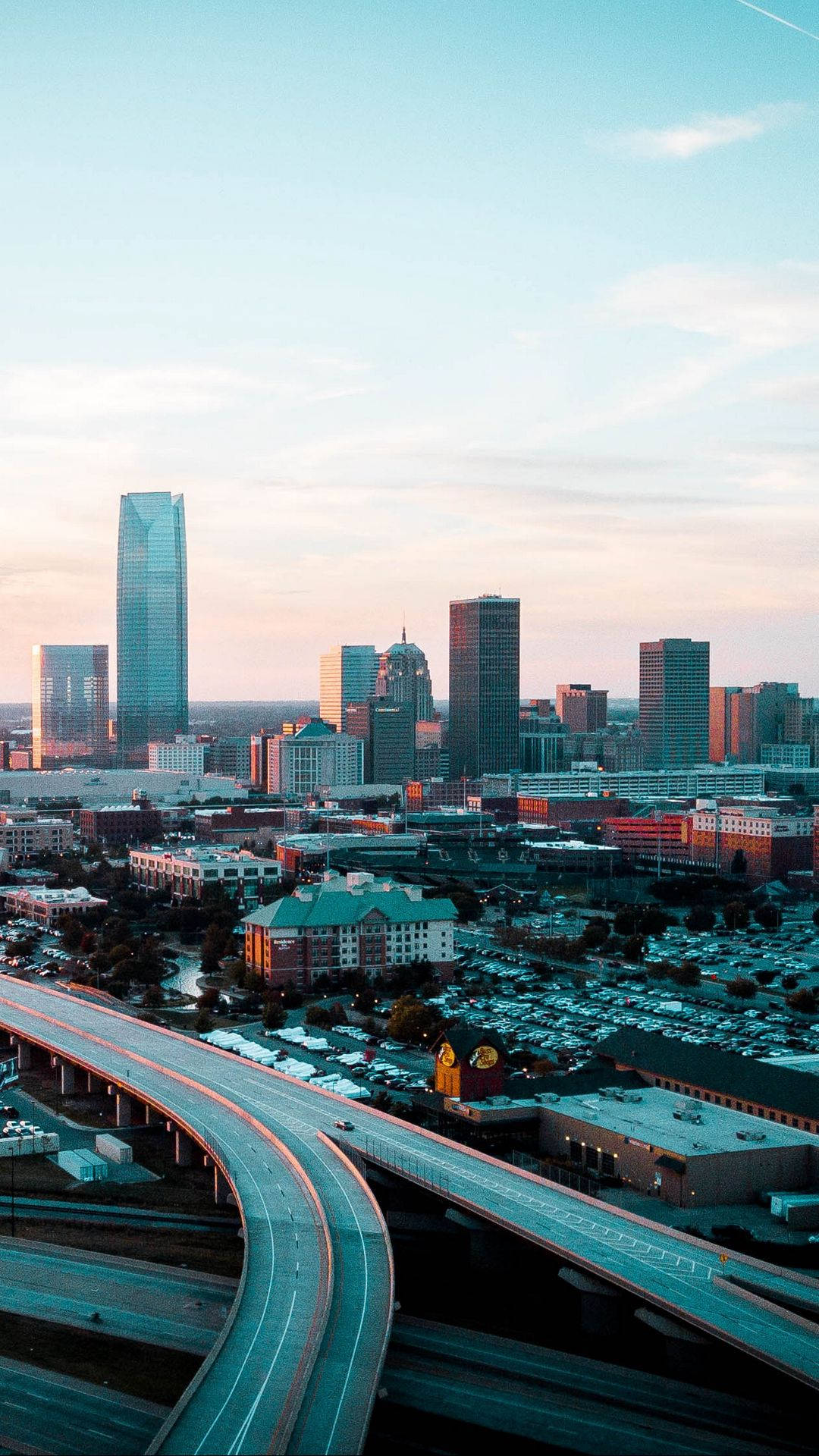 Oklahoma 桌布 壁紙 — 日落時分現代城市景觀的鳥瞰圖，蜿蜒的高速公路和高聳的摩天大樓沐浴在溫暖的金色光芒中。