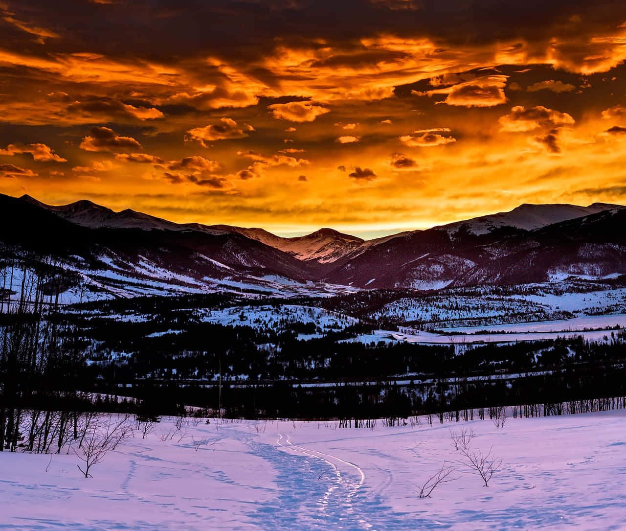 Colorado Mountain 桌布 壁紙 — 日落時分白雪覆蓋的山谷，暗黑山巒之上有火橙色雲彩，前景雪地上有蜿蜒的軌跡。