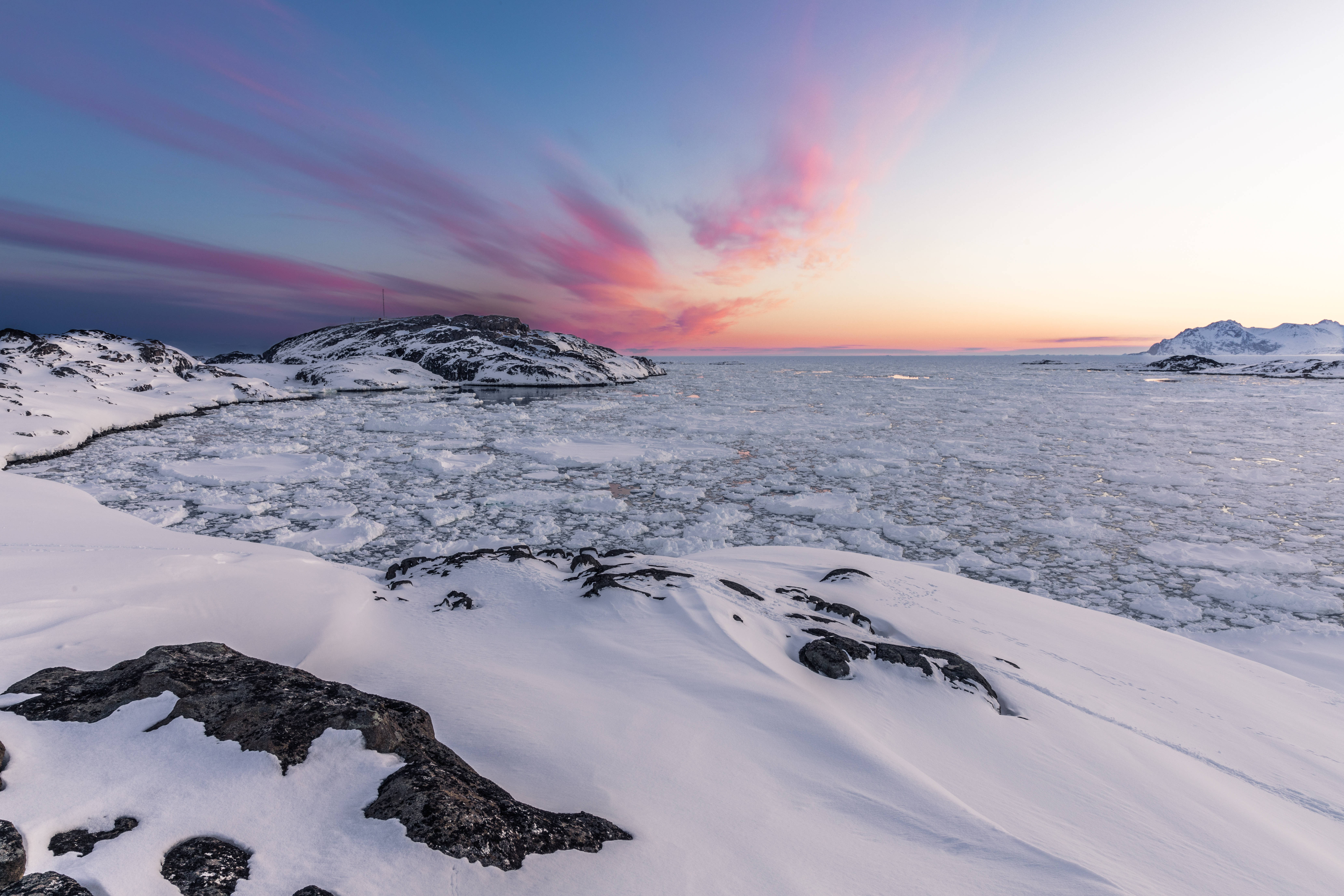 Greenland 桌布 壁紙 — 日落時分的冰封海岸景觀，雪覆蓋的岩石和浮冰在粉紅色和藍色雲彩的天空下。