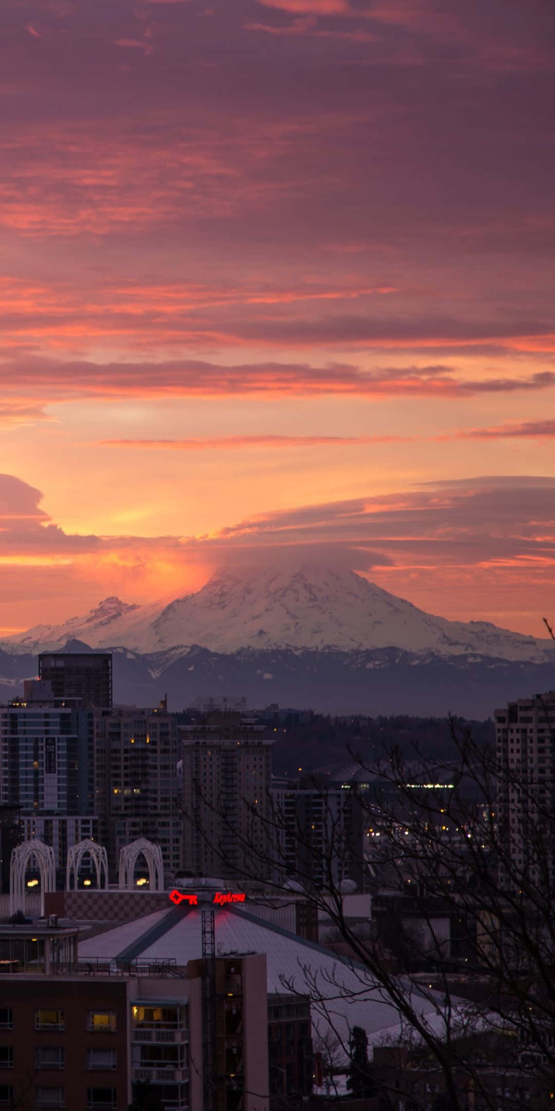 Pixel 3 Seattle 桌布 壁紙 — 日落時分的城市天際線，一座白雪覆蓋的山峰在火紅的橙色和粉紅色雲彩中閃耀。
