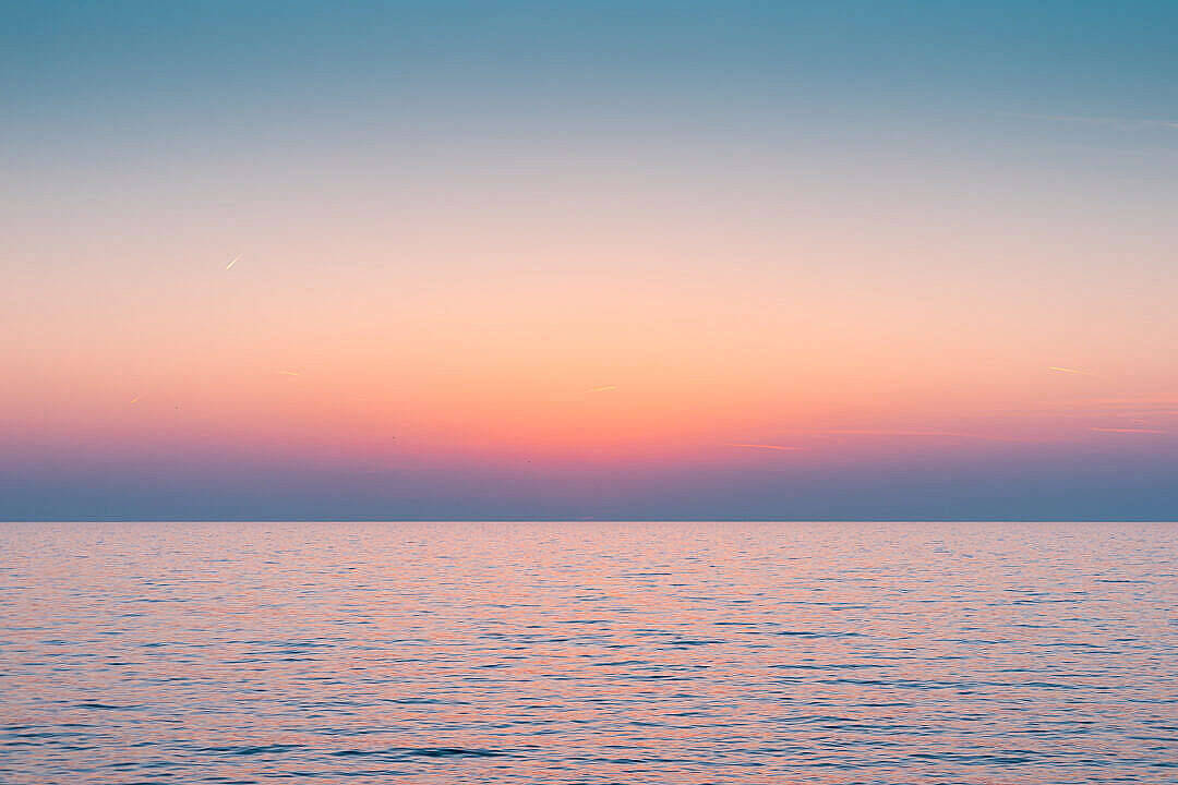 Calming 桌布 壁紙 — 日落時分的寧靜海洋，柔和的粉紅、橙色和藍色色調在地平線上交融。
