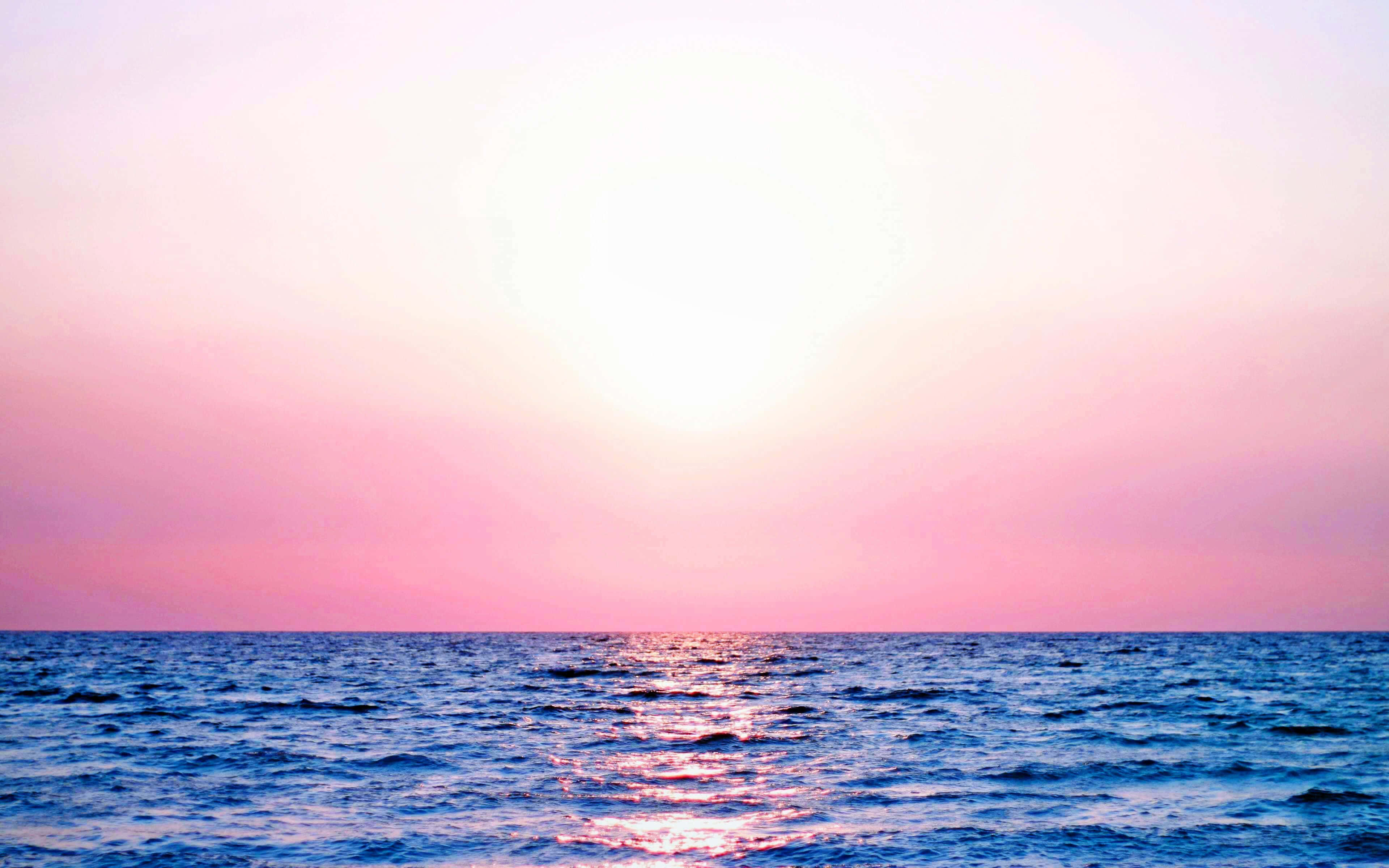 Calm Aesthetic Desktop 桌布 壁紙 — 日落時分的寧靜海洋，粉紅色的天空和發光的太陽映照在平靜的藍色波浪上。
