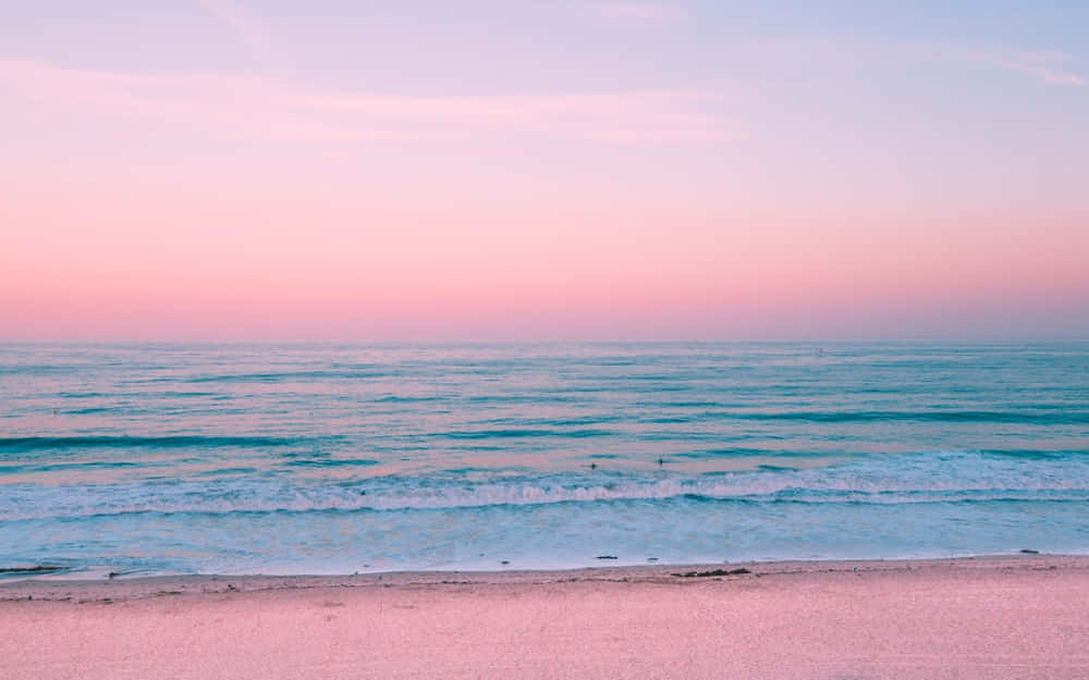 Pastel Beach 桌布 壁紙 — 日落時分的寧靜海灘，粉紅色的天空和藍綠色的海浪輕輕拍打著粉紅色的沙灘。